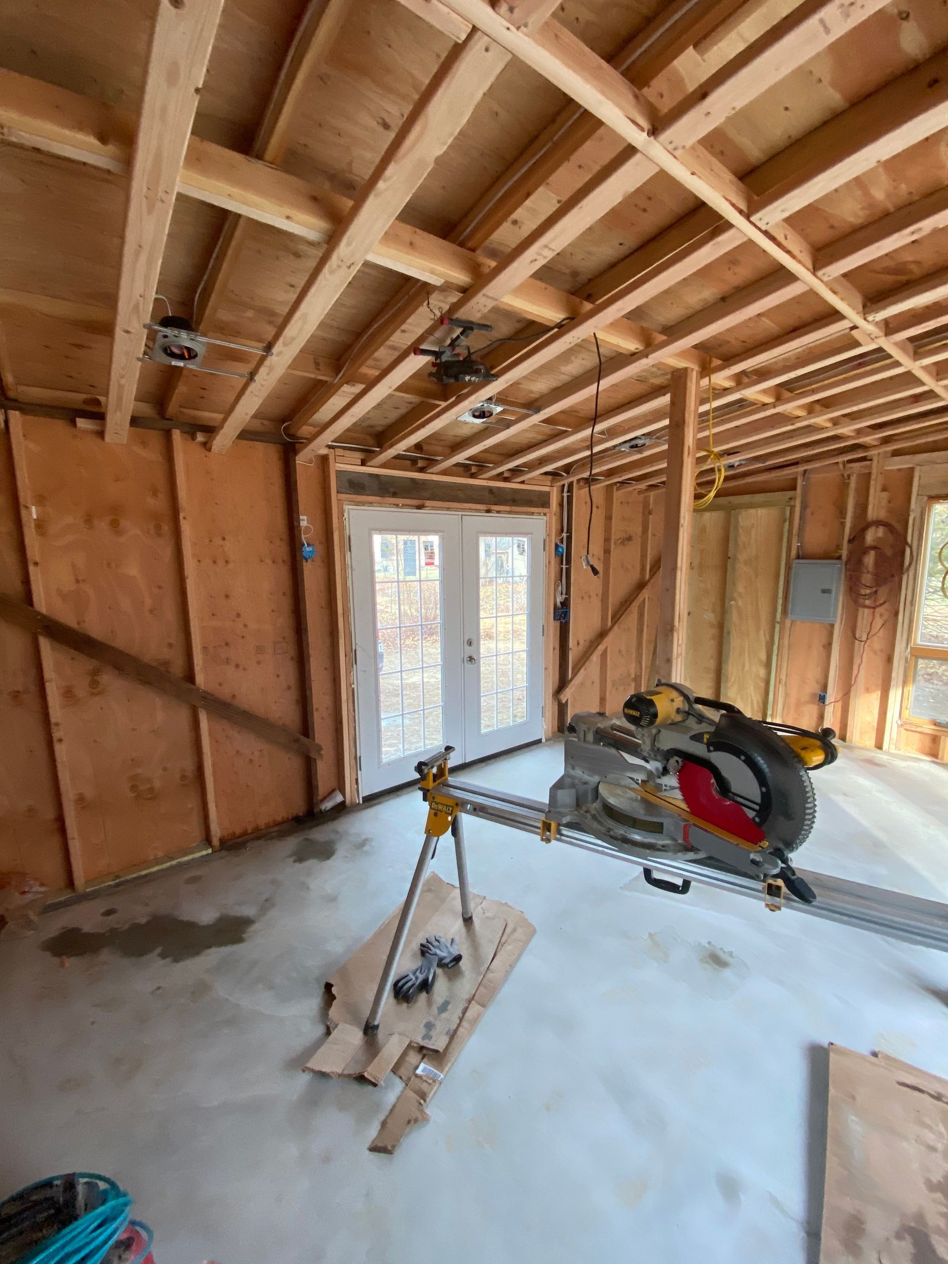 Unfinished room with exposed ceiling beams, drywall, a window, and a saw on the floor.