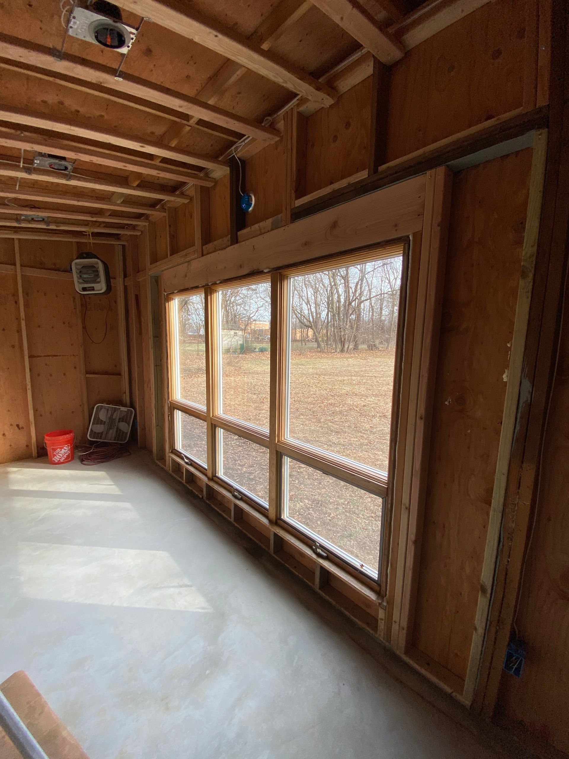 Empty unfinished room with exposed wood walls, large windows, and a concrete floor.