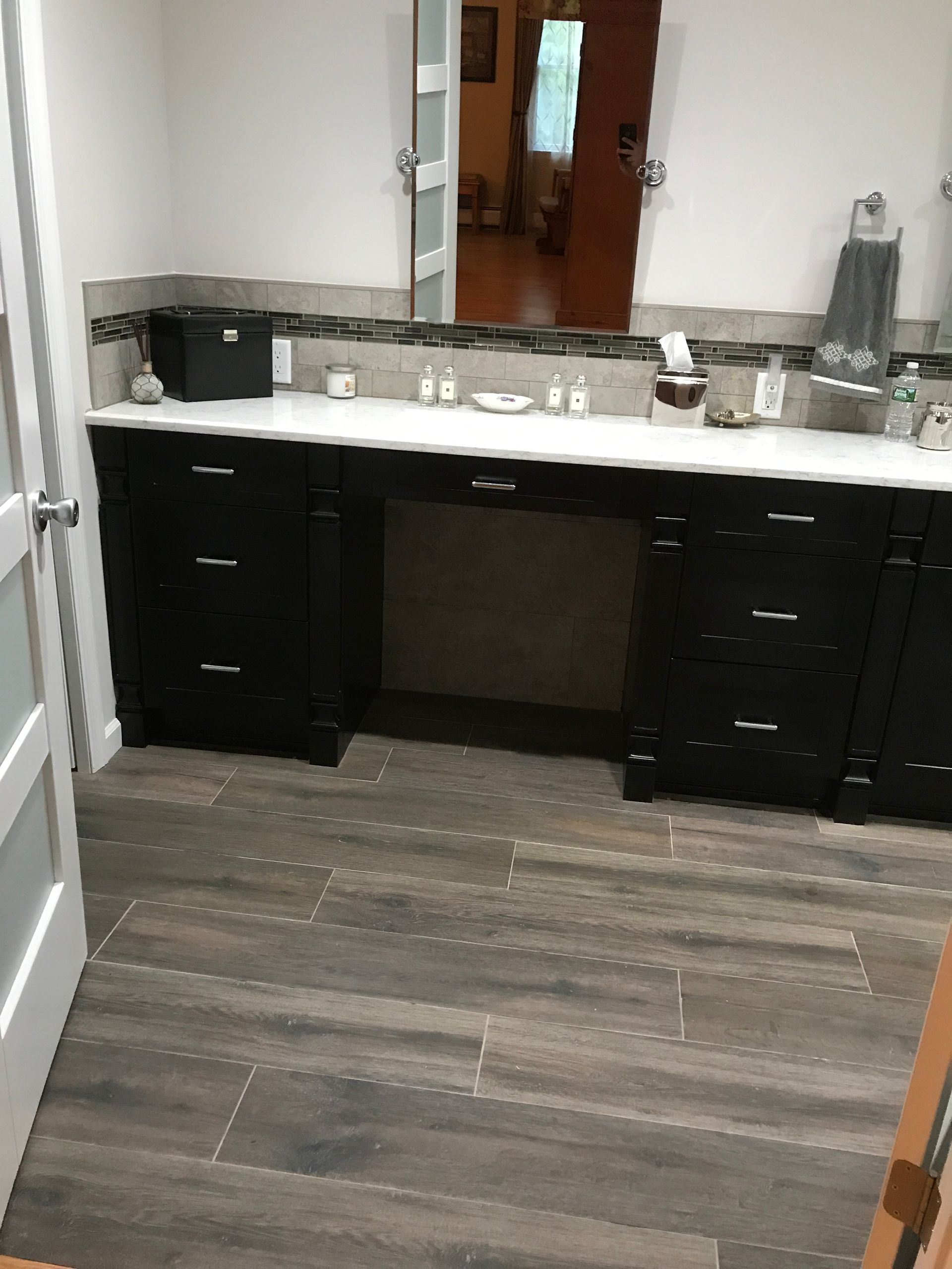 Bathroom vanity with black cabinets, gray countertop, and a wall mirror above wood-look flooring