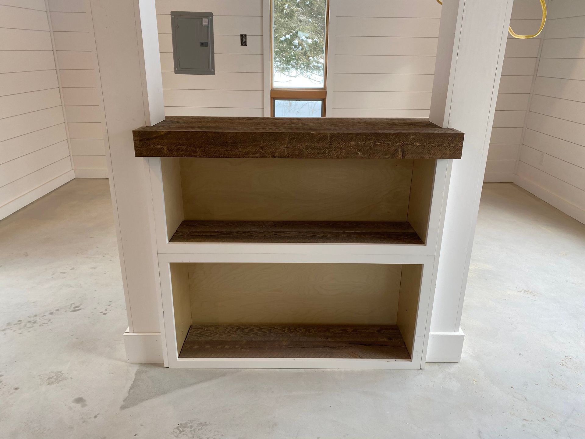 White built-in shelving unit with dark wood counter in a small room, white shiplap walls and floor.
