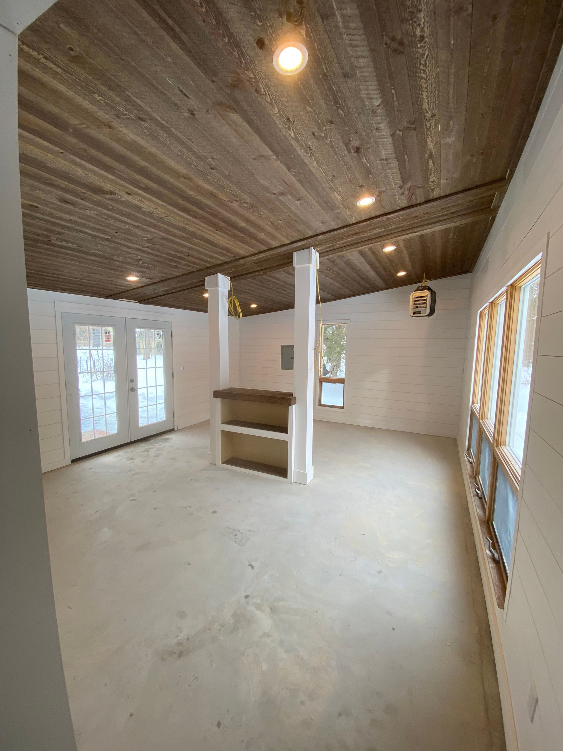 Empty unfinished room with white walls, exposed wood ceiling, and French doors on the left.