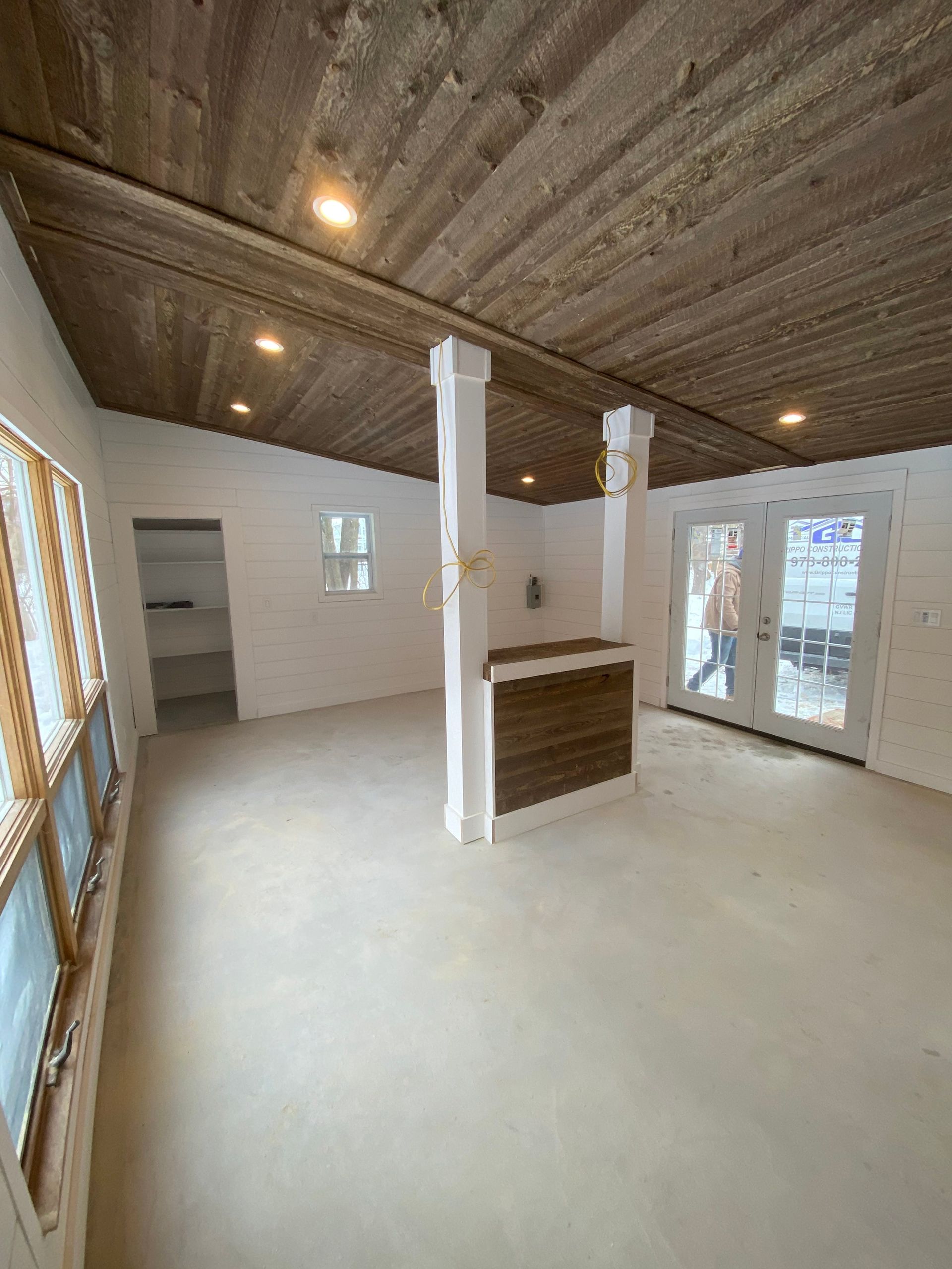Empty room with white walls, wood ceiling, central white pillar, and double glass doors opening outside.