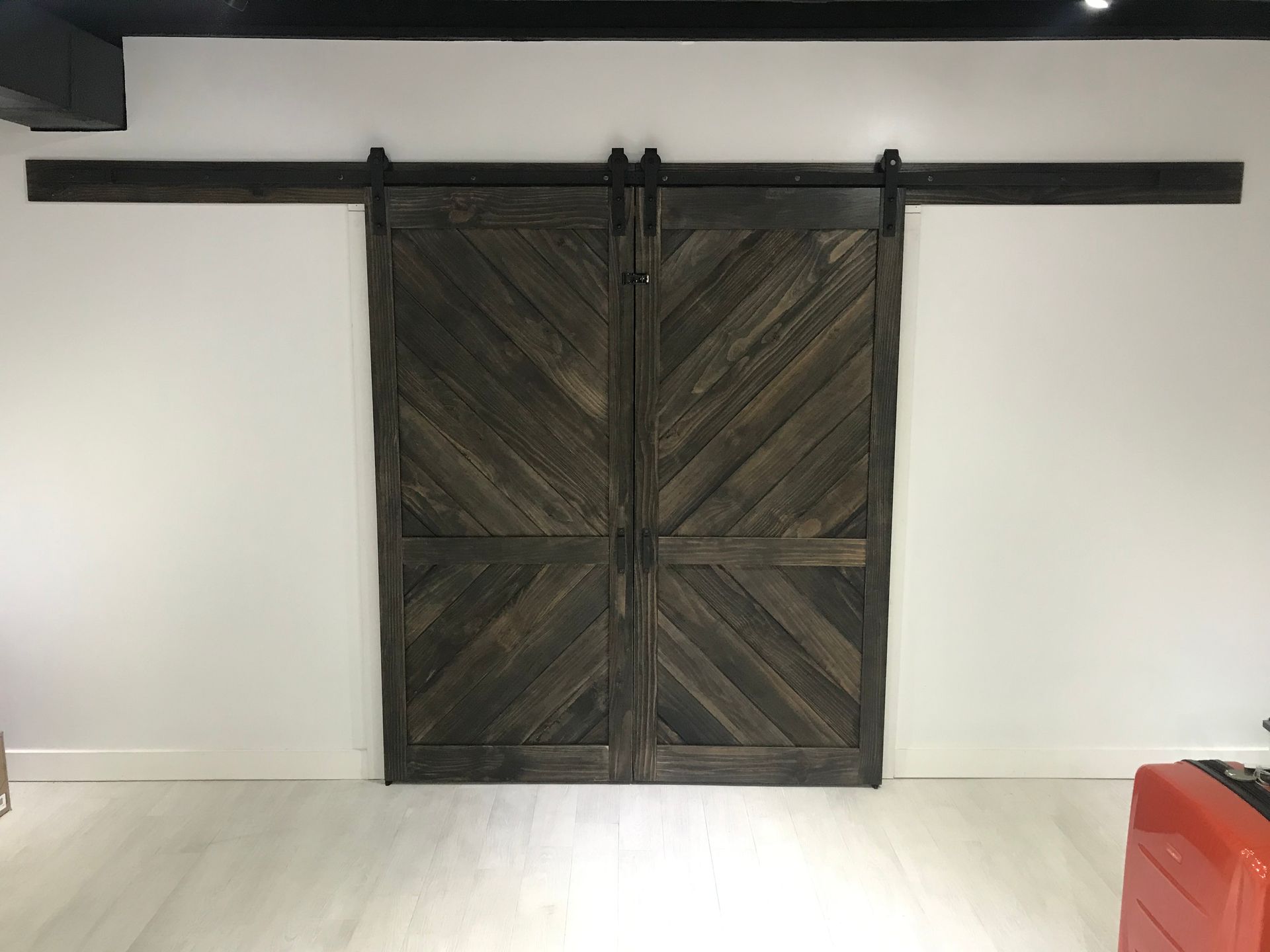 Rustic dark wood sliding barn doors on a white wall with a black rail above and pale floor below