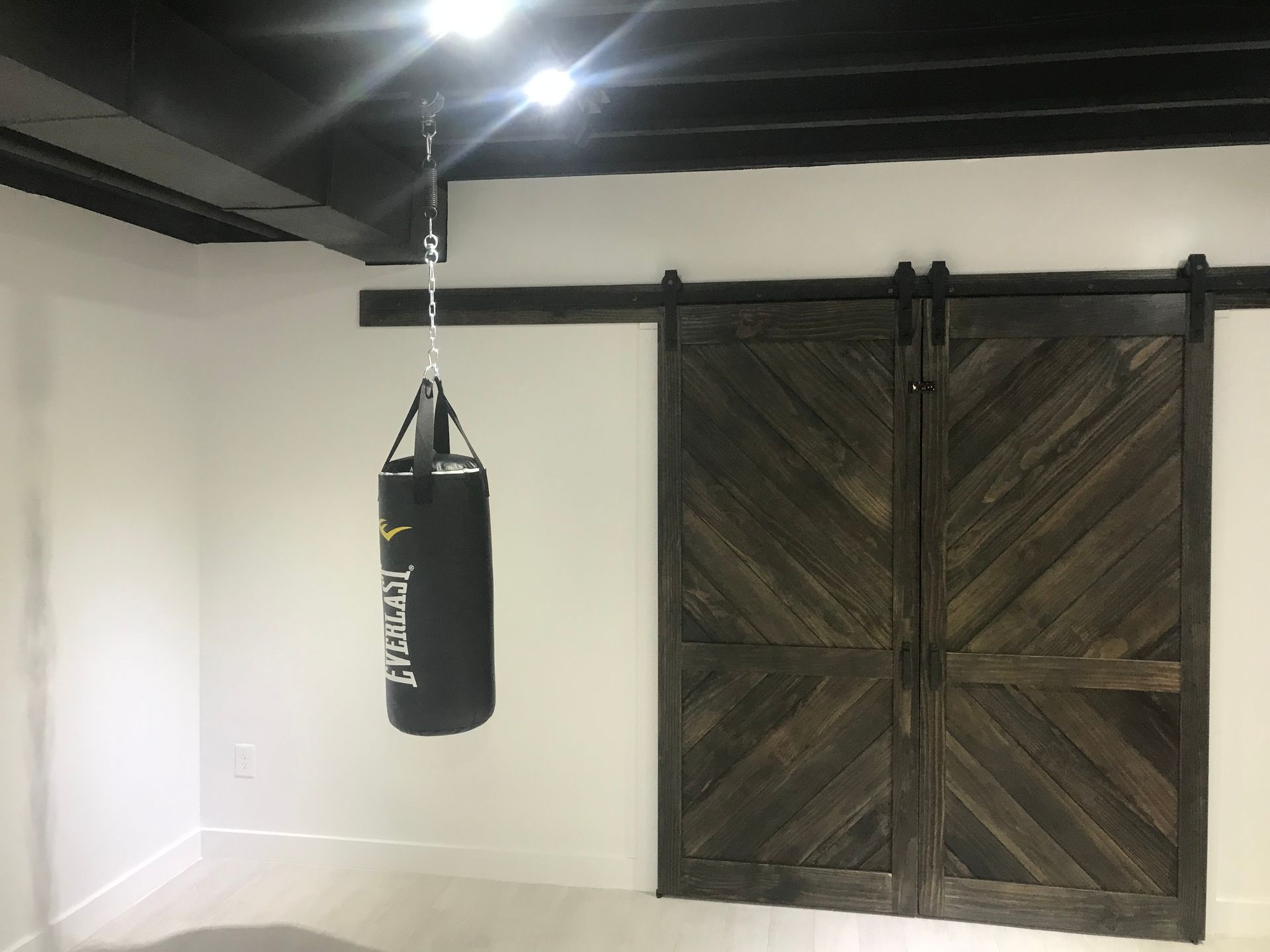Small indoor gym with a hanging black punching bag and dark wooden sliding doors.