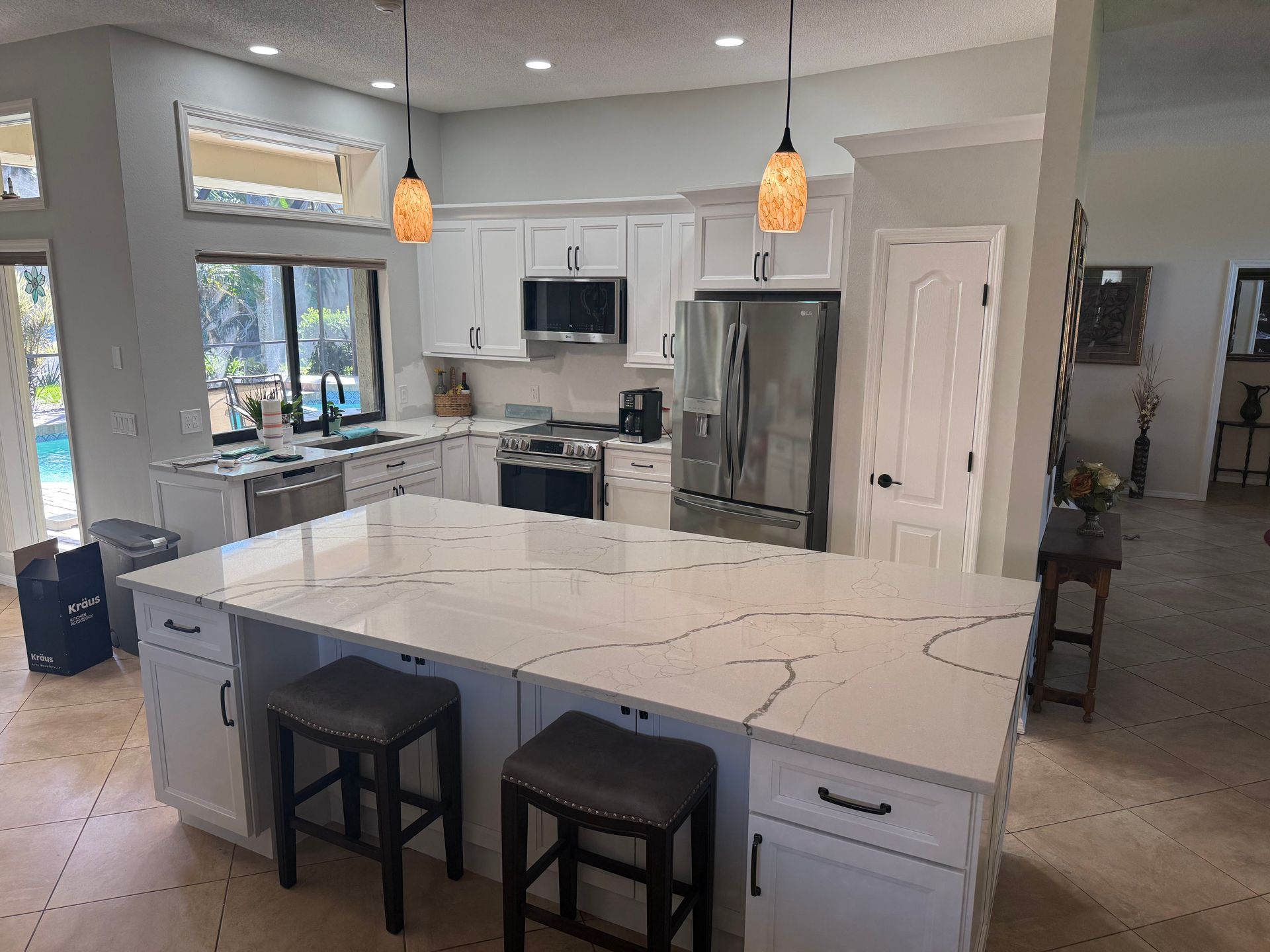 Modern kitchen with white cabinets, large island, stainless steel appliances, and two black stools