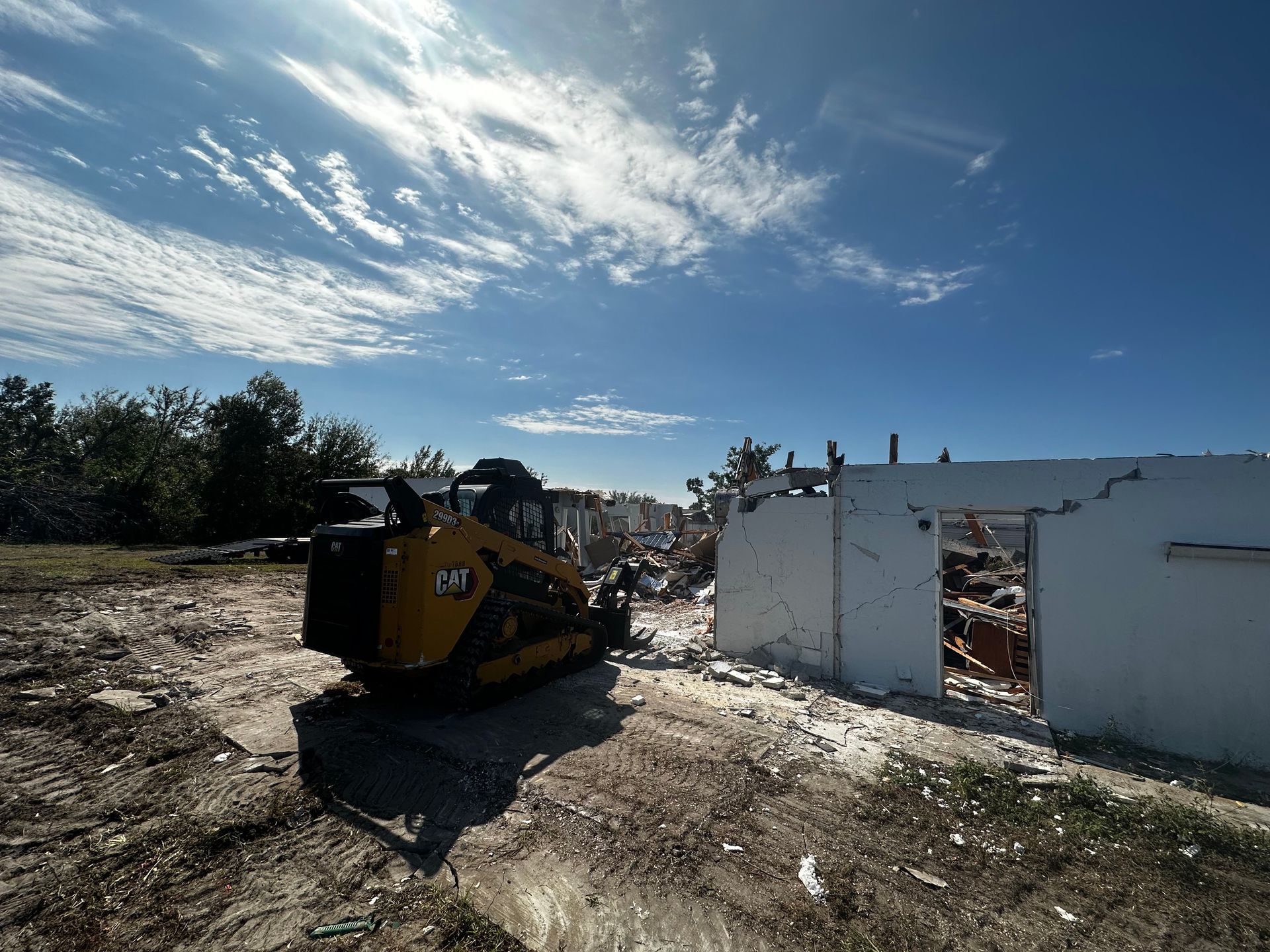 Yellow construction vehicle beside a damaged white building under a bright blue sky