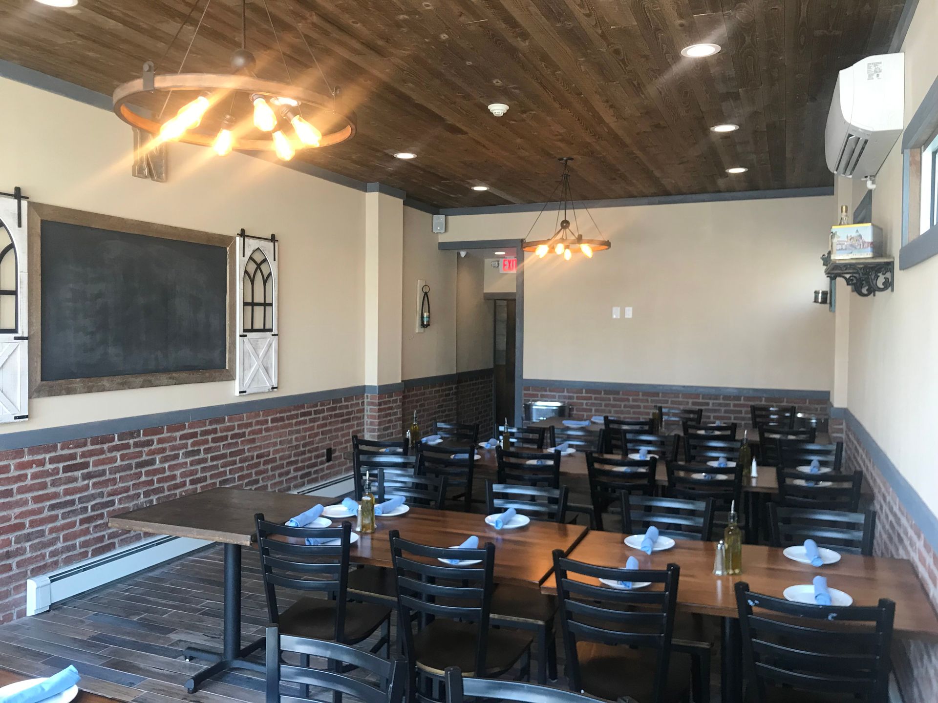 Empty restaurant dining room with black tables and chairs, brick walls, and wooden ceiling lights
