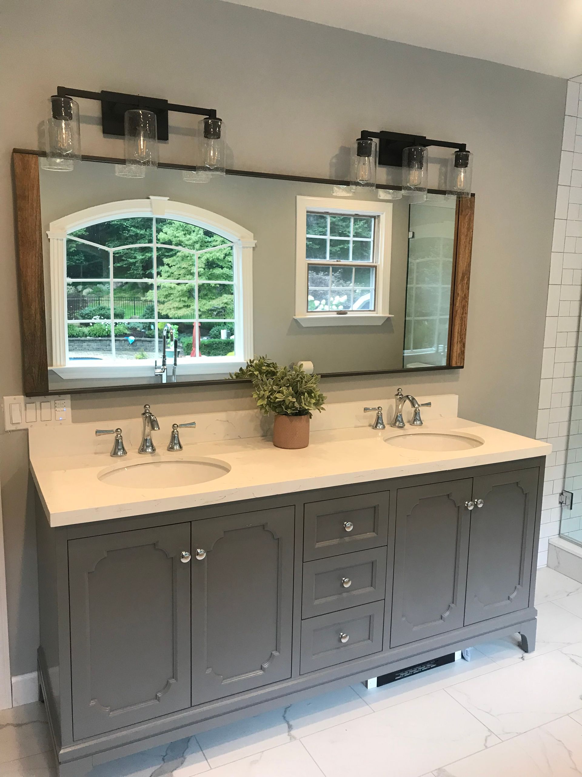 Double vanity bathroom with gray cabinets, white countertop, mirrors, and windows above sinks