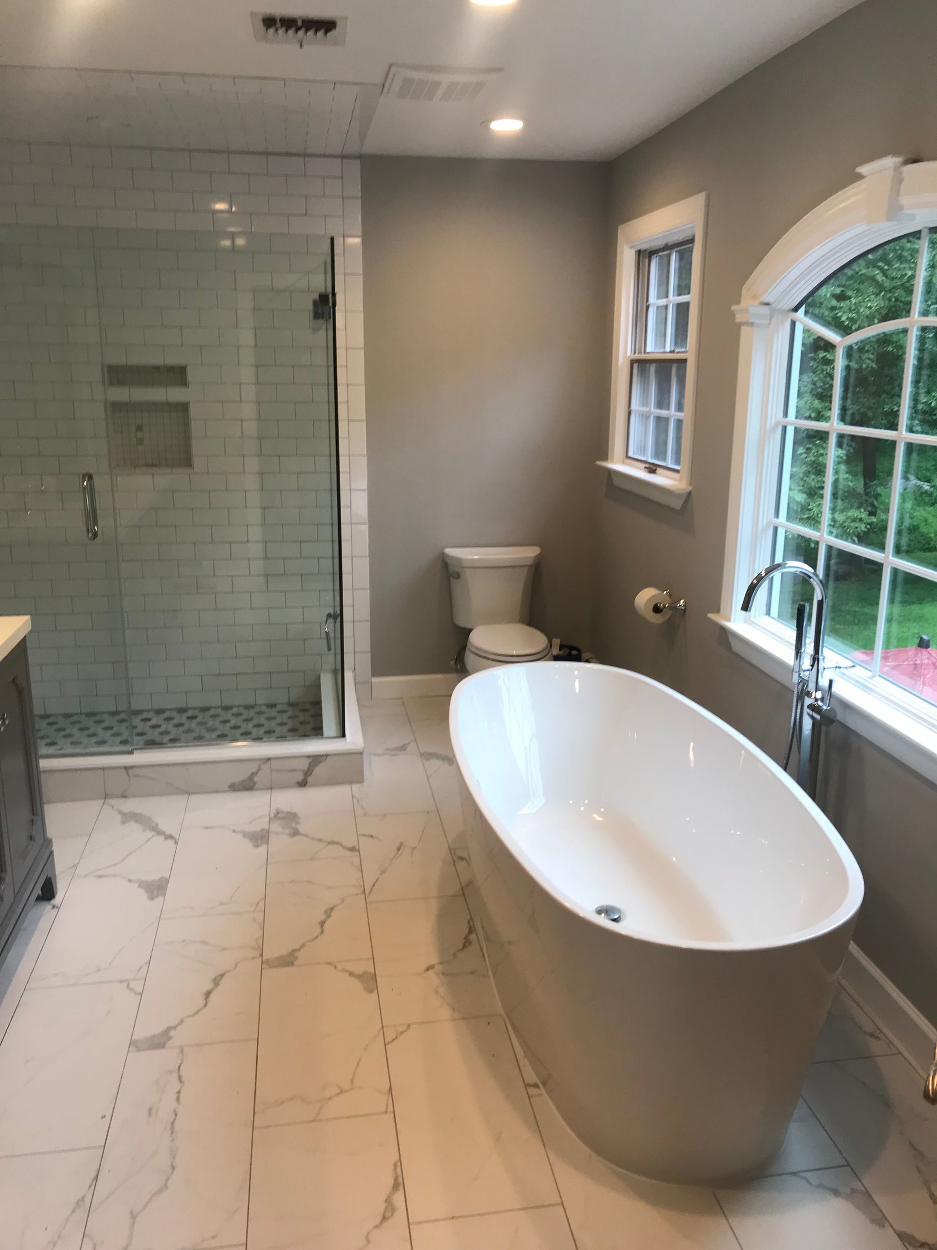 Modern bathroom with freestanding tub, glass shower, toilet, and white marble tile floor