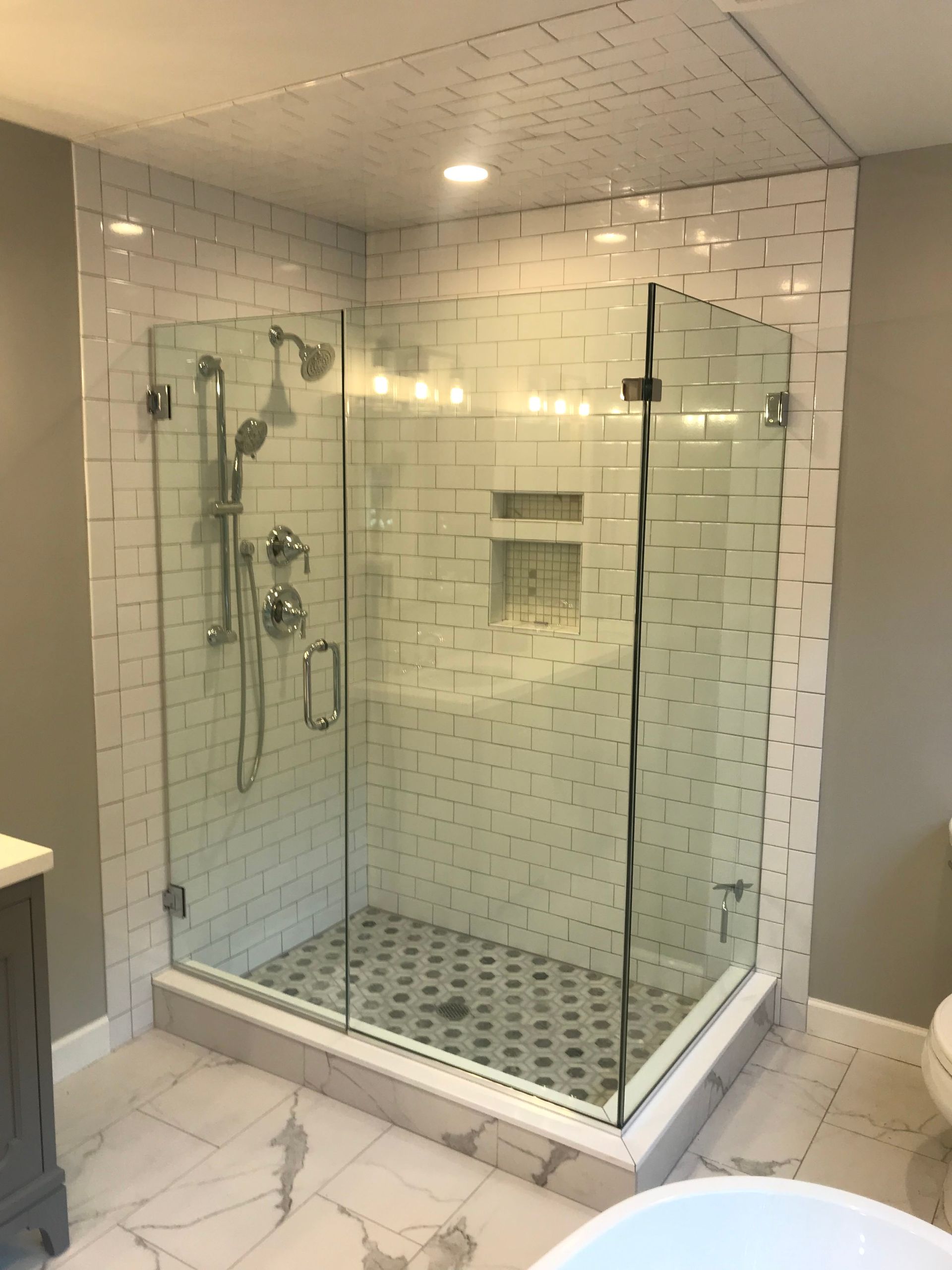Glass walk-in shower with white subway tile, showerhead, handheld sprayer, and pebble mosaic floor