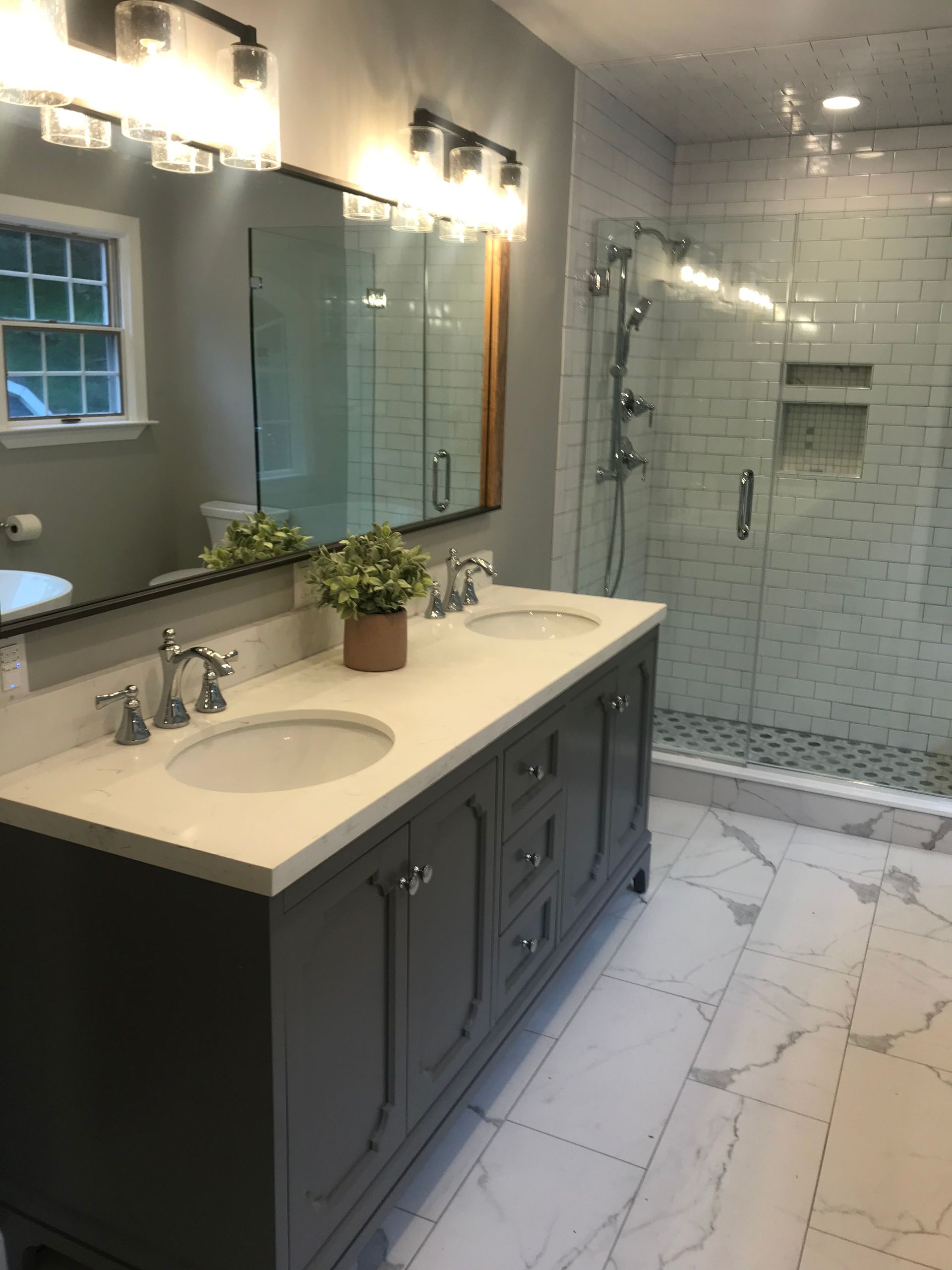 Modern bathroom with double sink vanity, large mirror, glass shower, and white marble tile flooring