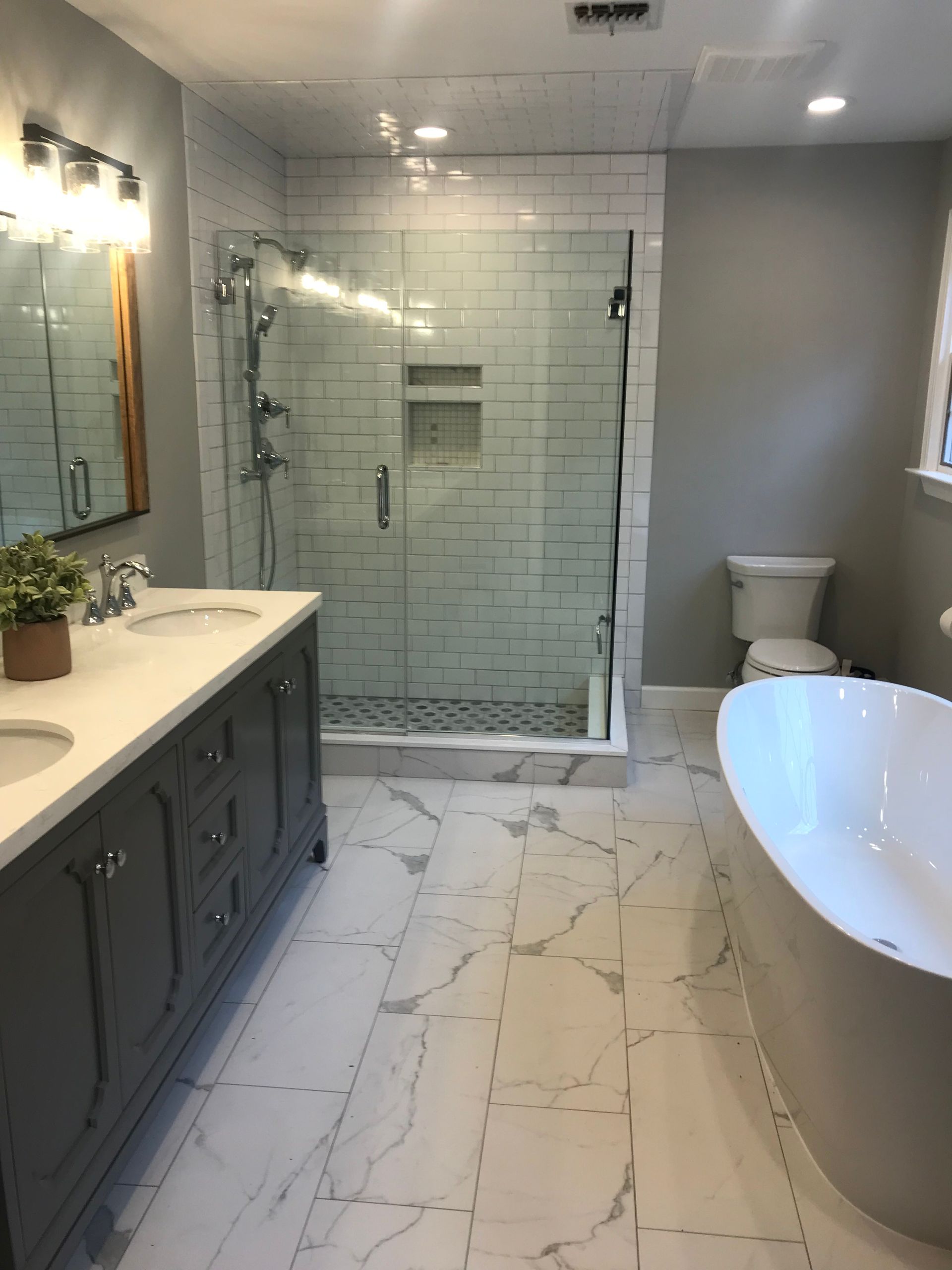 Modern bathroom with glass shower, double vanity, and freestanding tub on marble-look tile floor