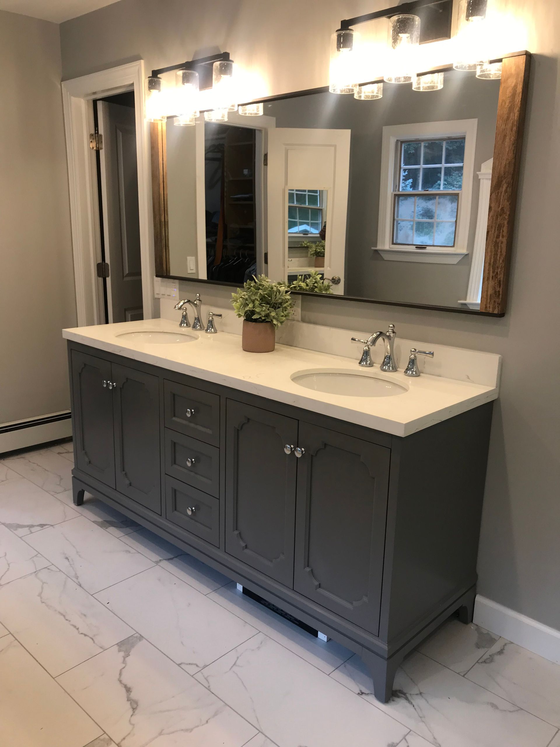 Bathroom vanity with double sinks, dark cabinets, large mirror, and wall sconces in a bright tiled room