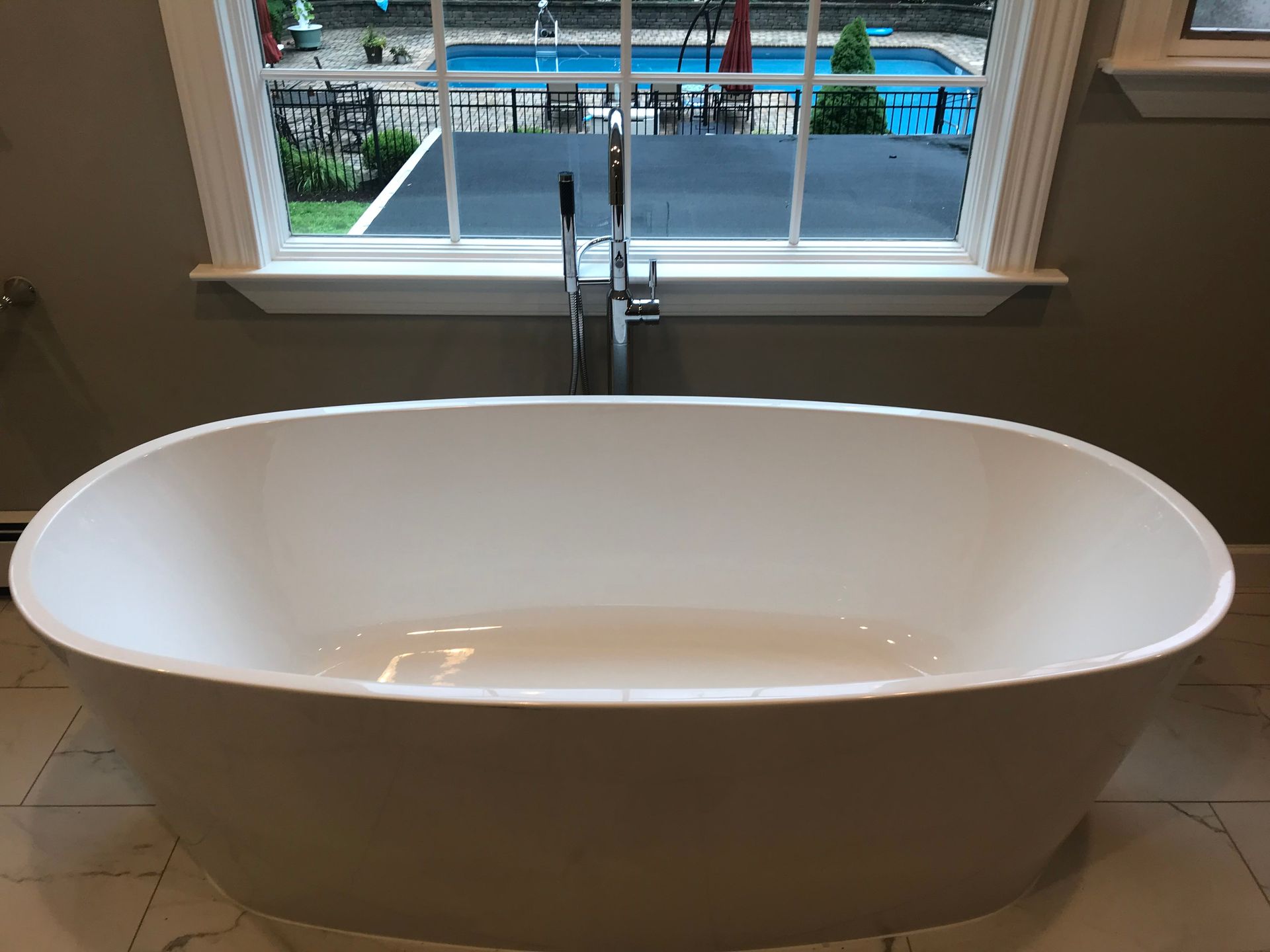 Freestanding white bathtub in front of a window with a chrome faucet