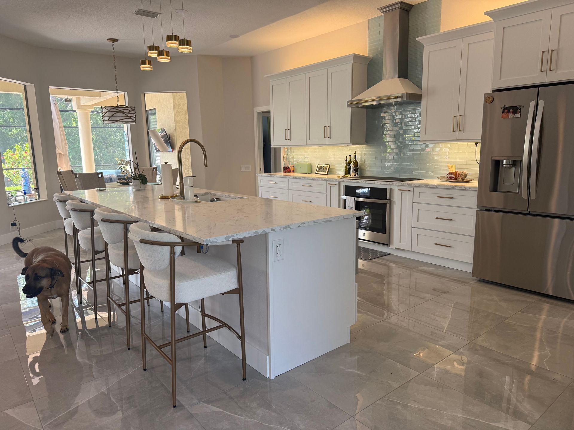 Bright modern kitchen with marble island, stainless appliances, and a dog near the dining chairs