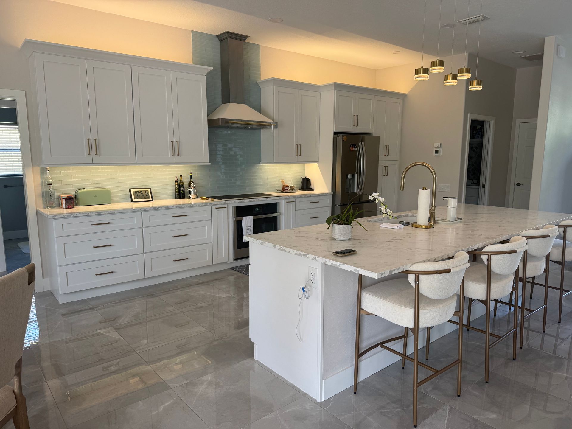 Modern white kitchen with island, bar stools, gray tile floor, and stainless steel appliances
