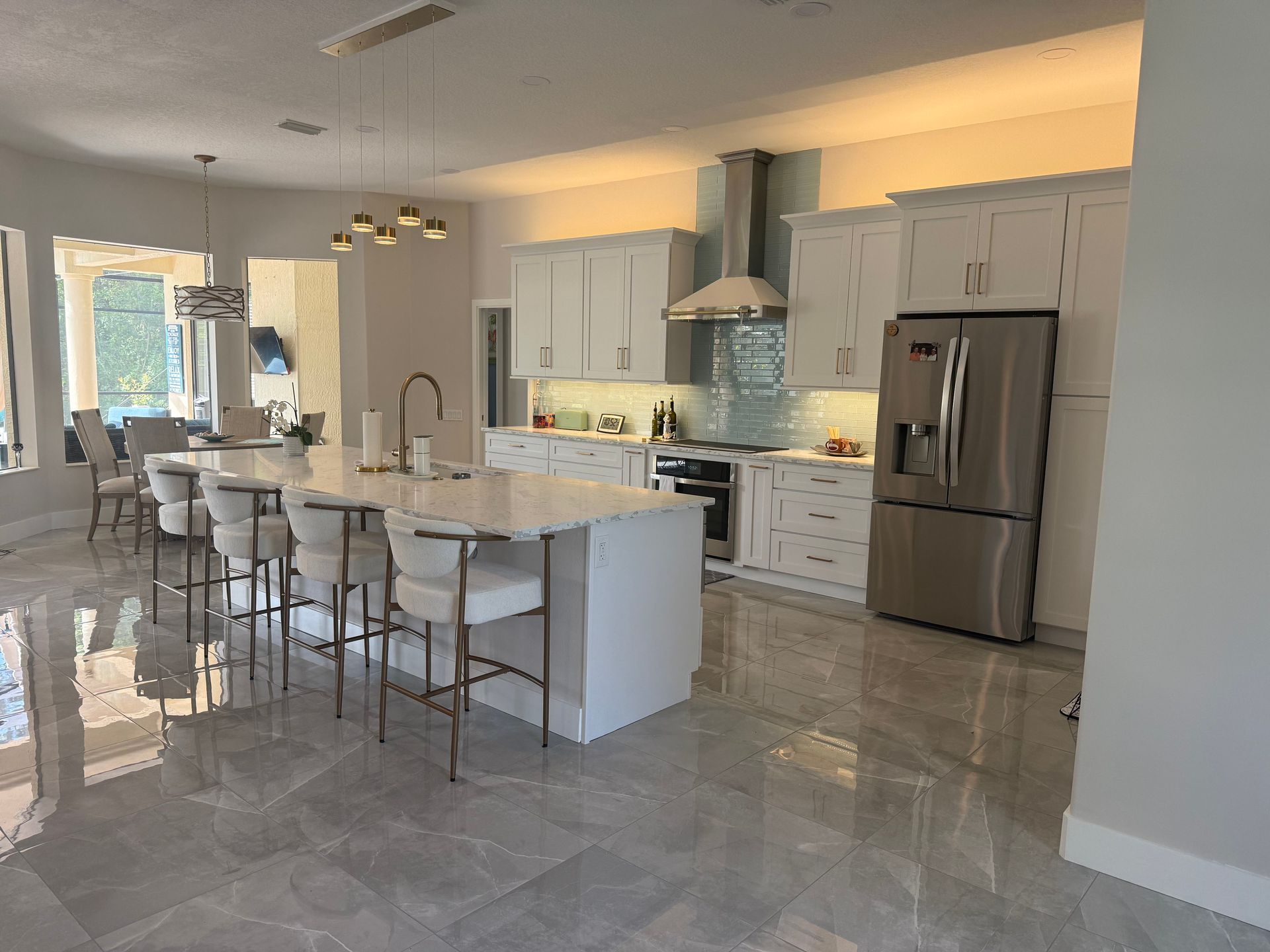 Bright modern kitchen with white cabinets, stainless fridge, island seating, and glossy tile floors