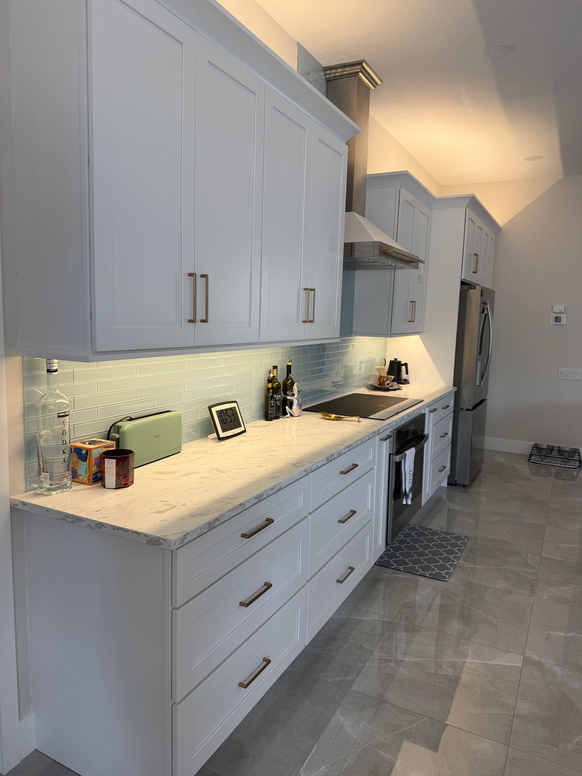 Bright white kitchen with cabinets, stone countertop, and appliances along a narrow hallway.