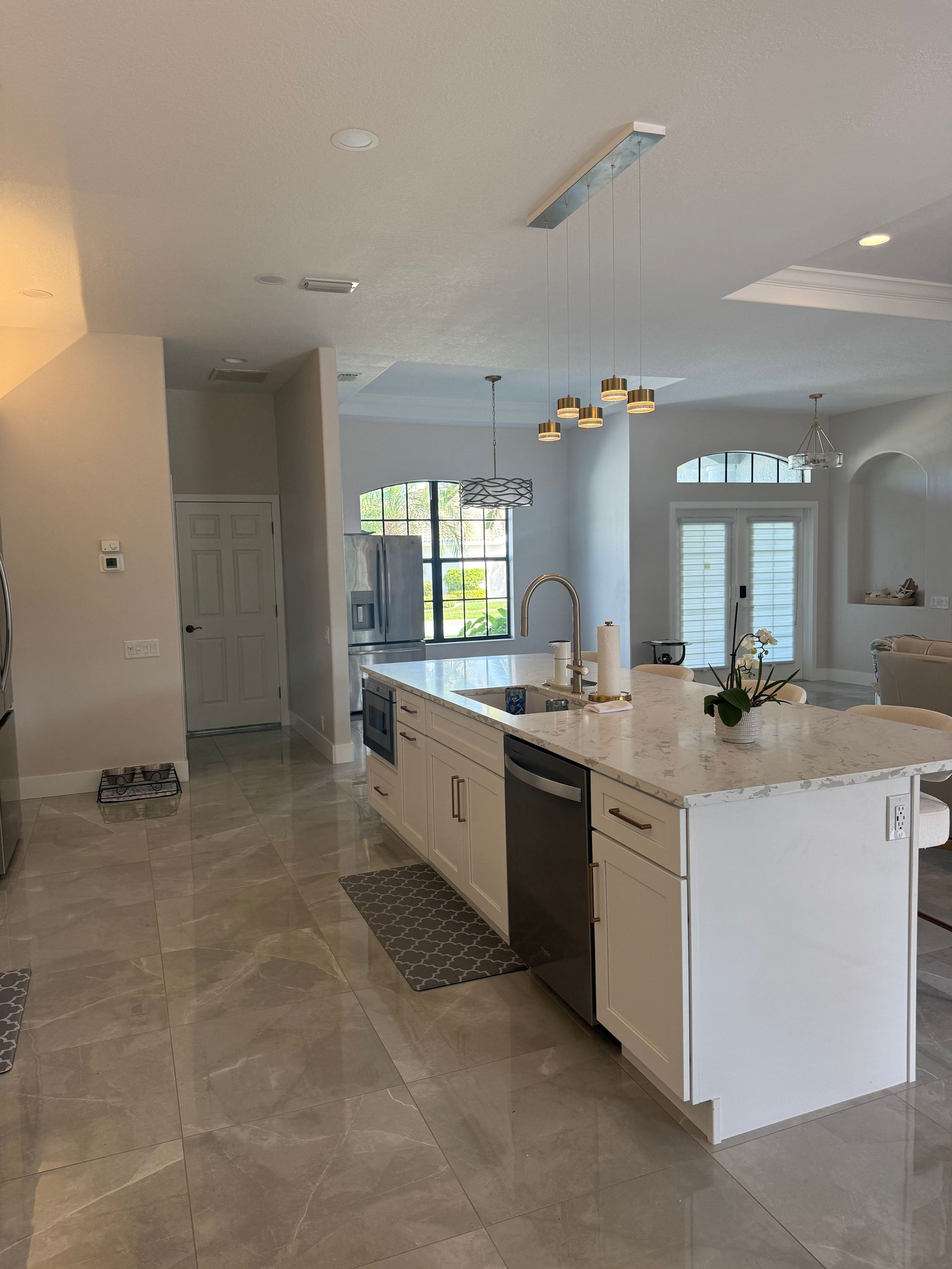 Bright modern kitchen with white cabinets, island, pendant lights, and tiled floor