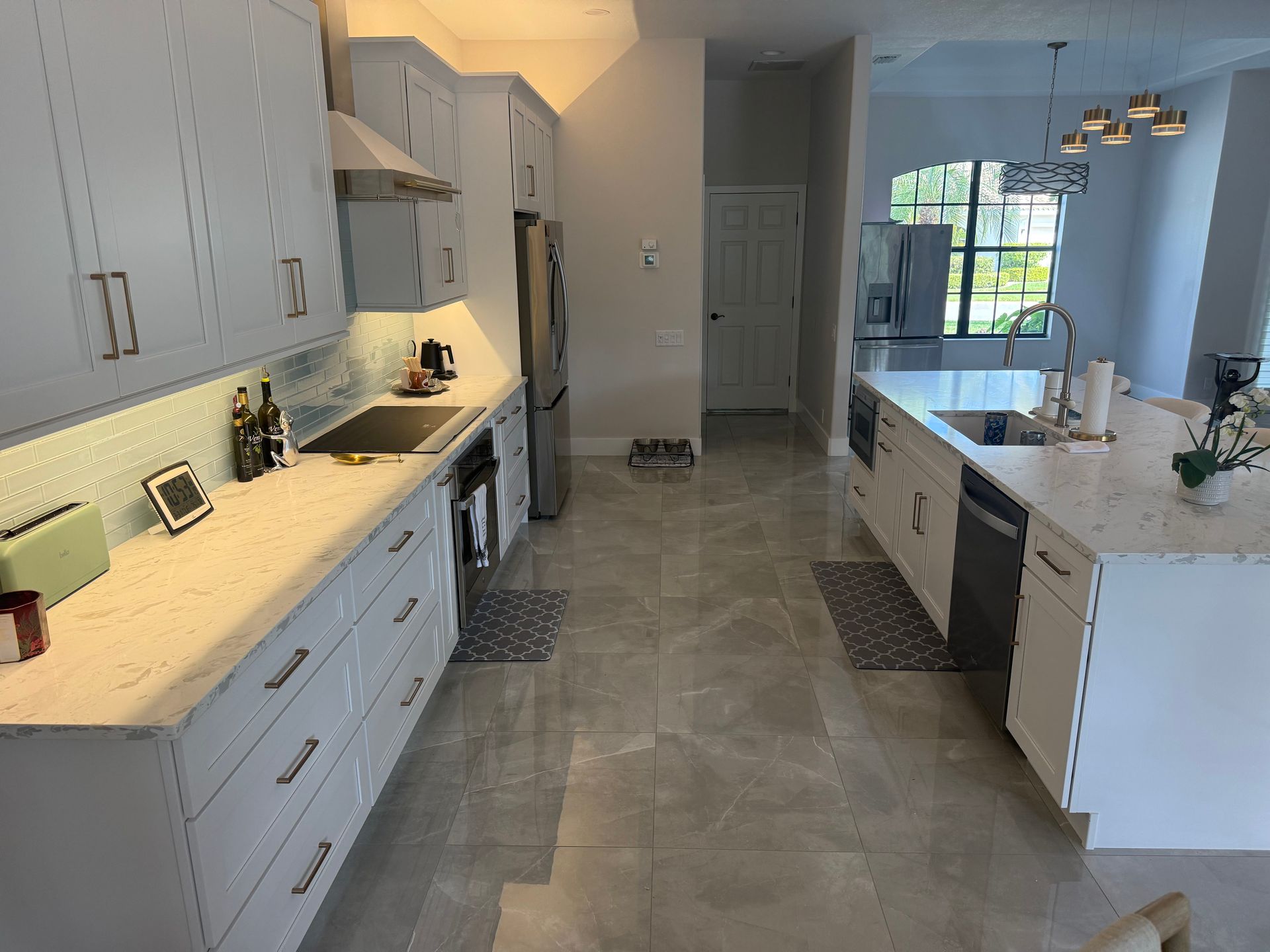 Bright modern kitchen with white cabinets, island, gray tile floor, and large window at the back