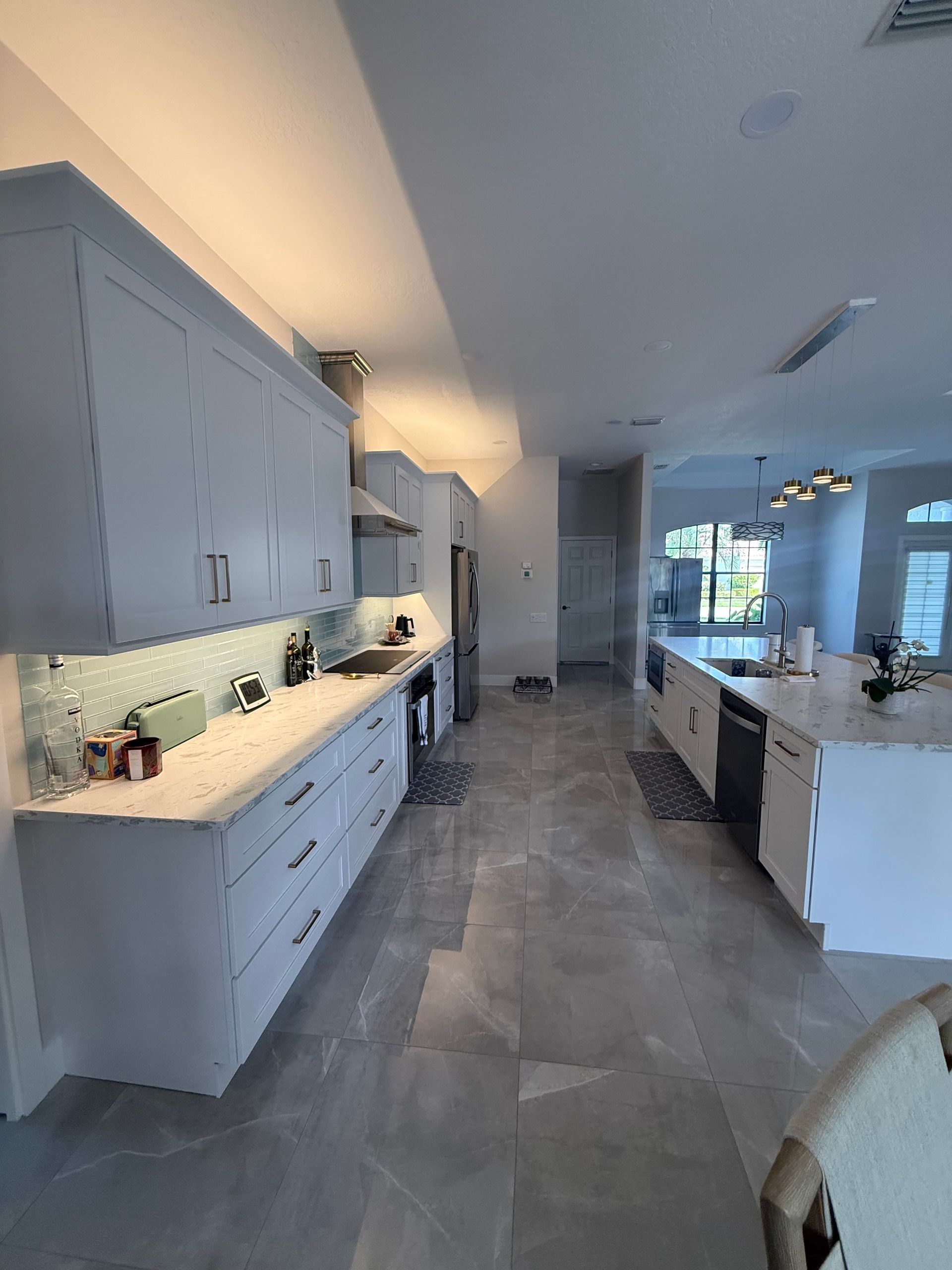Bright modern kitchen with white cabinets, gray tile floor, and large windows overlooking a pool