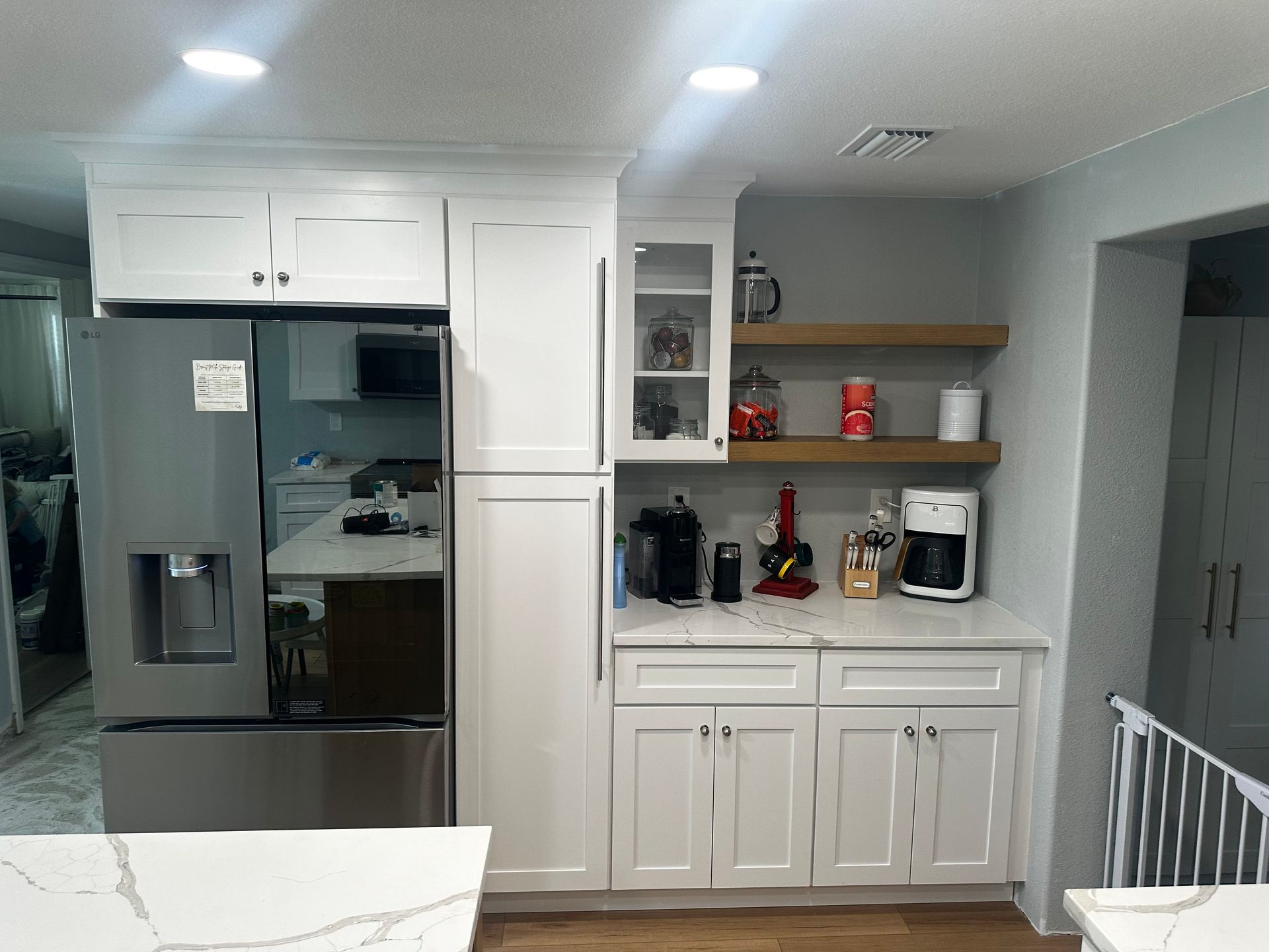 White kitchen with stainless fridge, white cabinets, coffee station, and counter seating area.