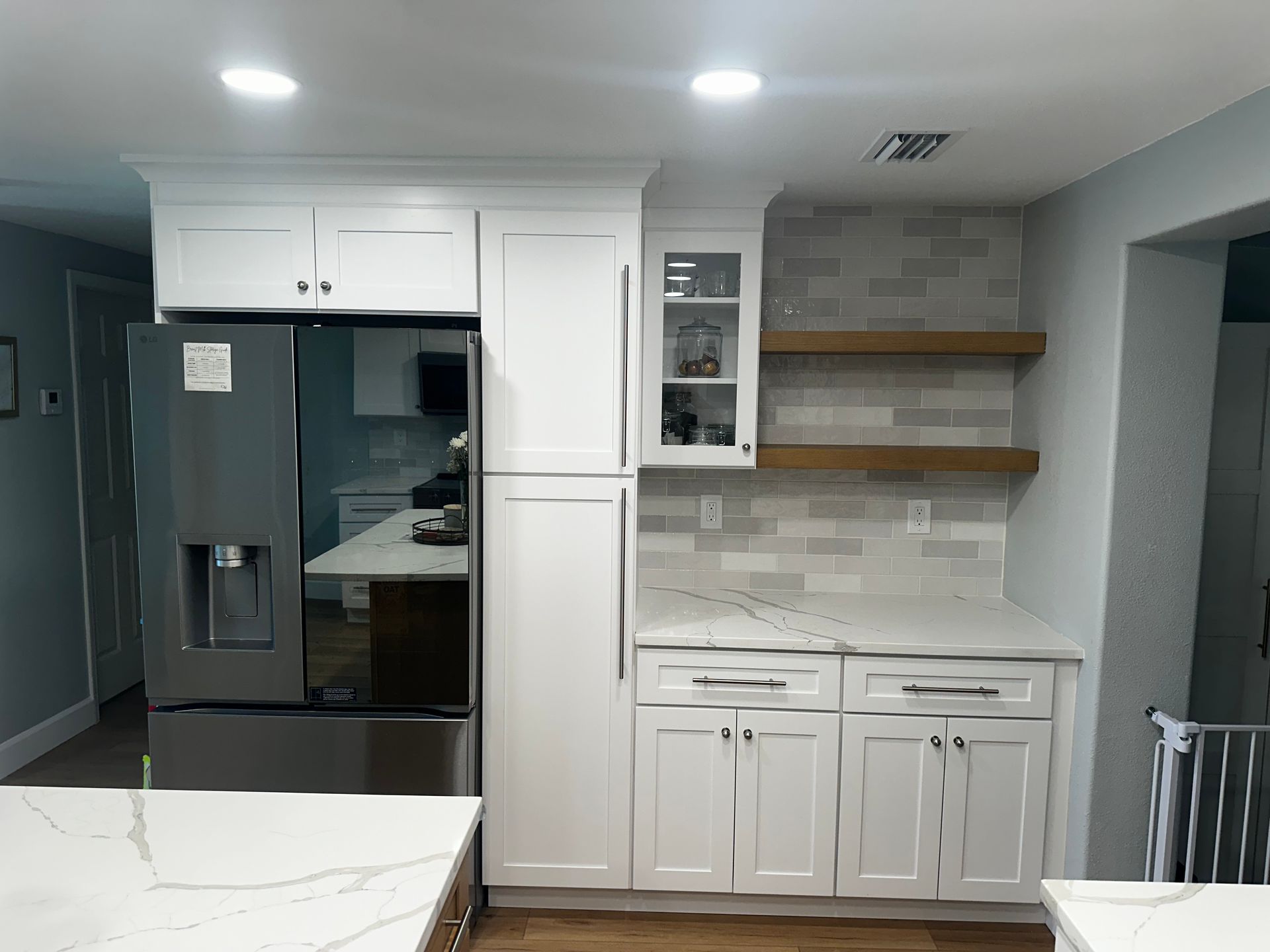 Modern kitchen with white cabinets, dark refrigerator, and open shelves on a gray wall