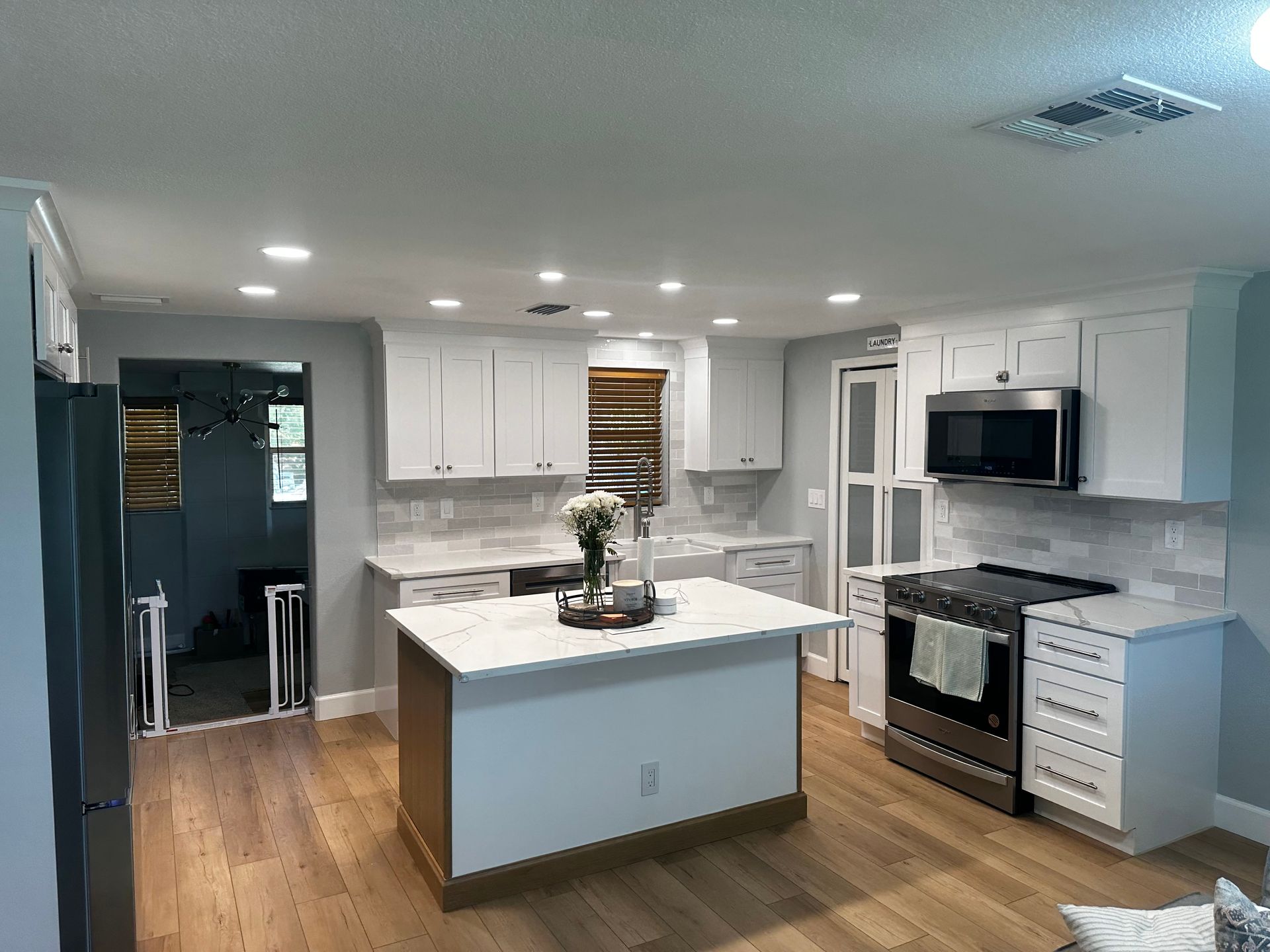 Bright modern kitchen with white cabinets, gray island, stainless appliances, and wood floors
