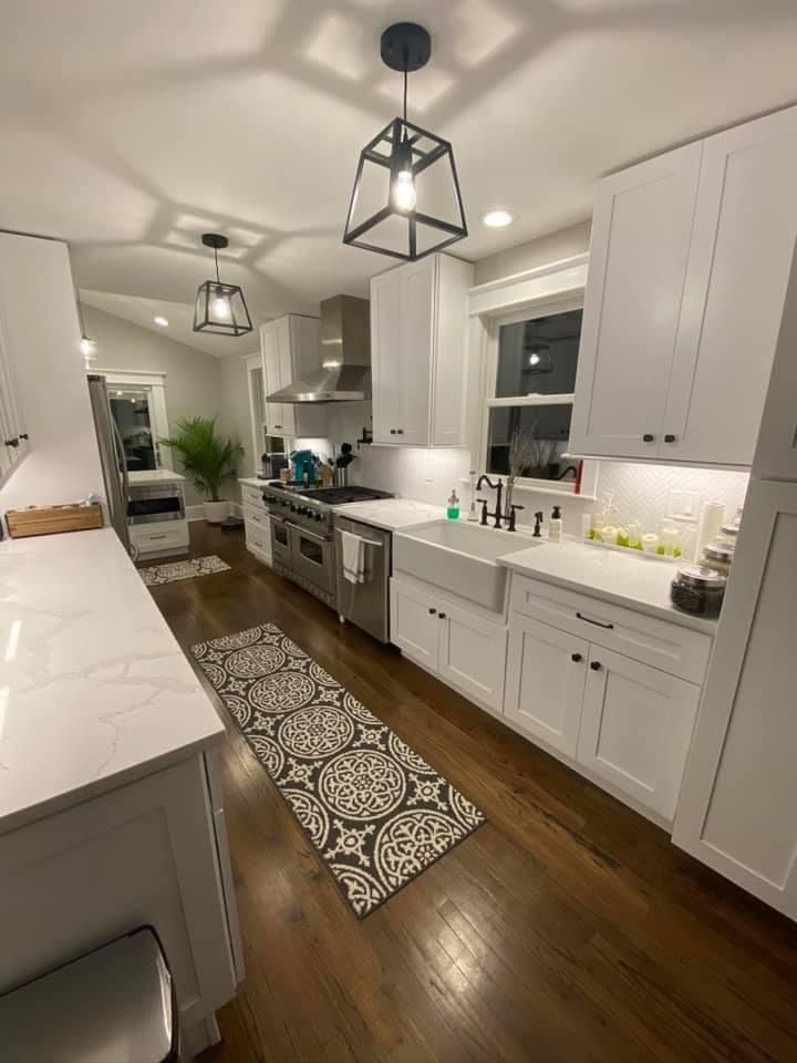 Bright modern kitchen with white cabinets, stainless appliances, wood floors, and patterned runner rug