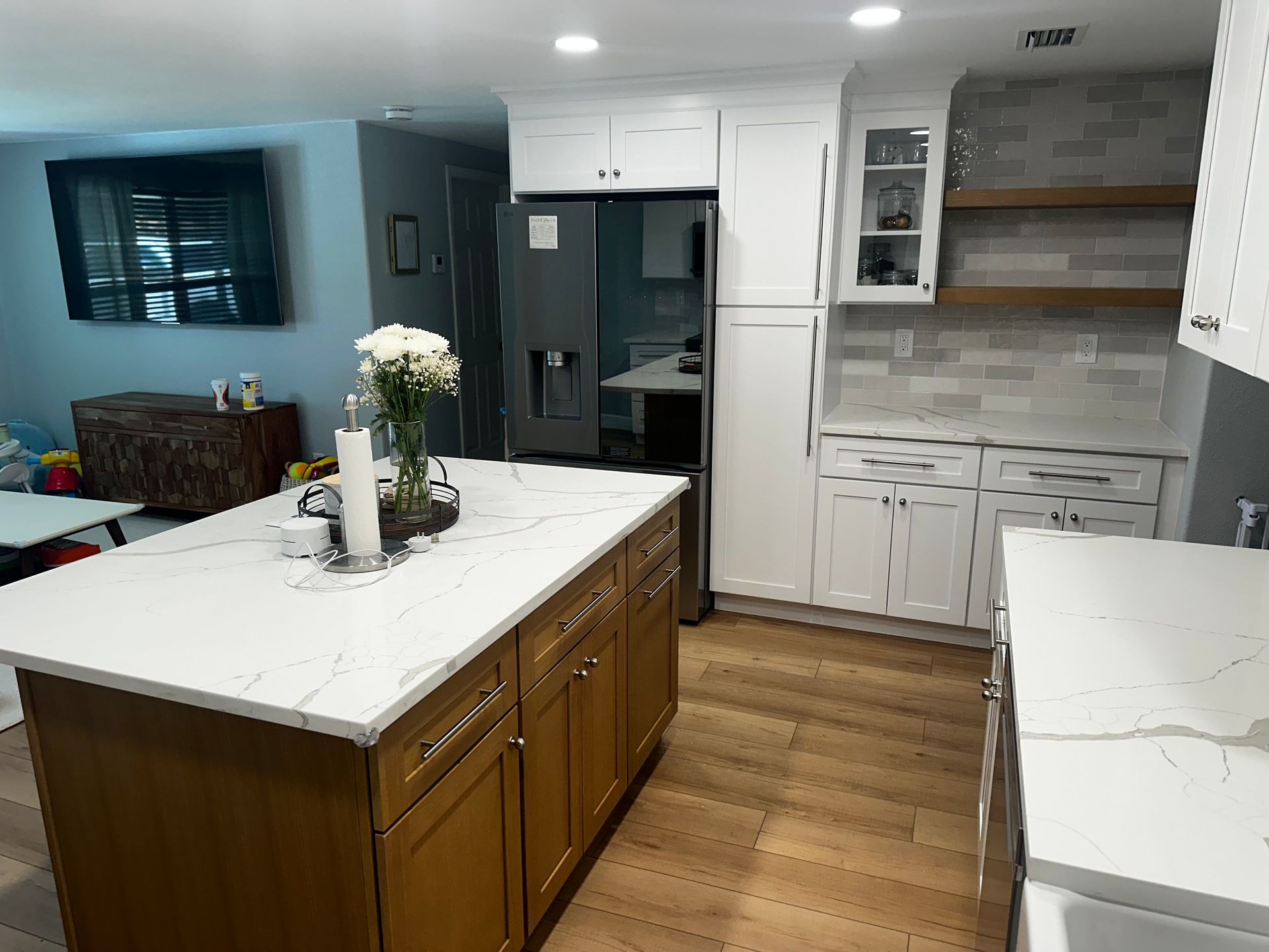 Bright modern kitchen with white cabinets, wood island, stainless fridge, and marble countertops