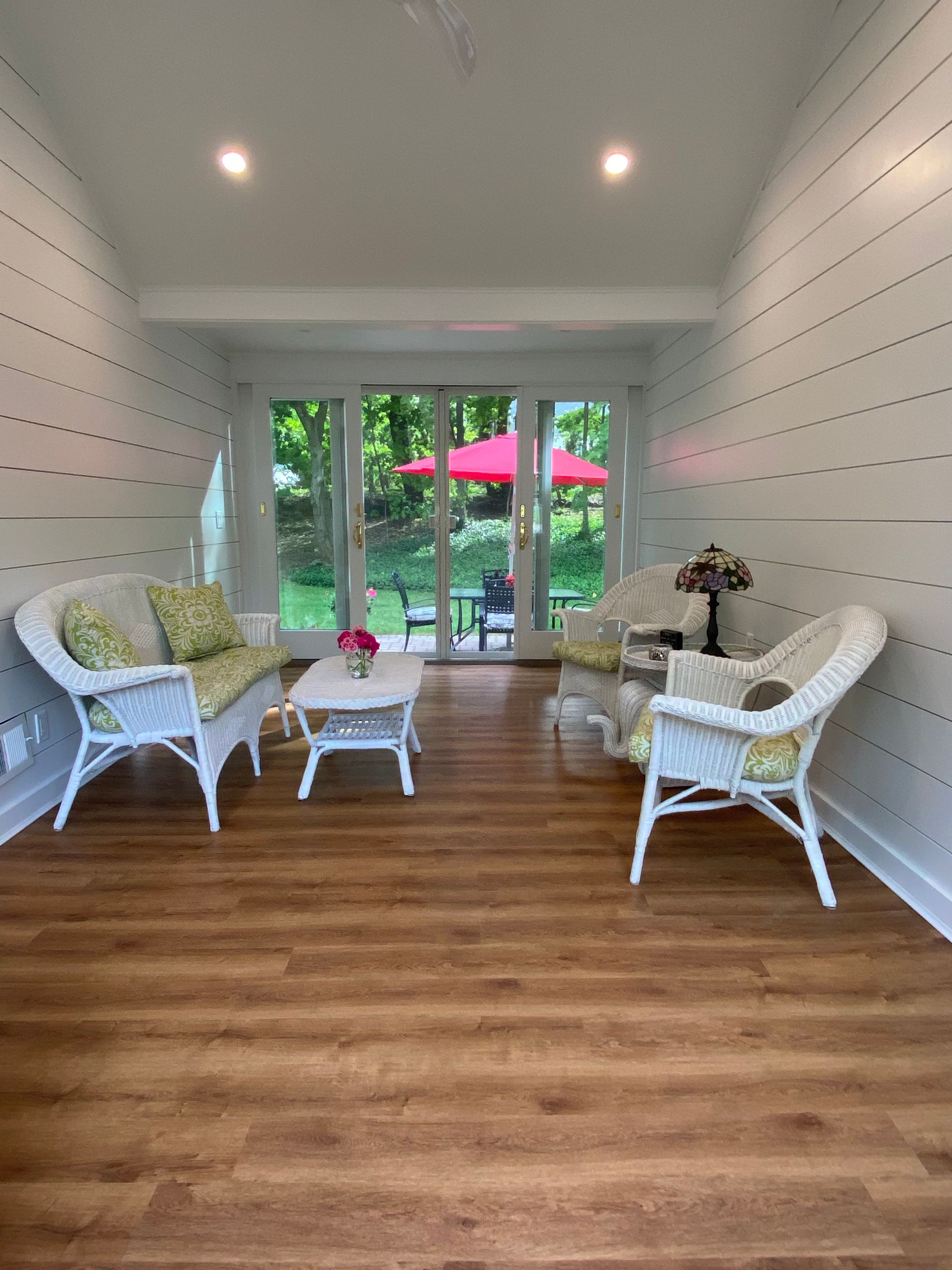 White wicker seating area with coffee table in a bright sunroom opening to a garden patio