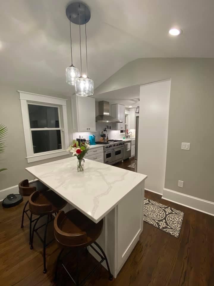 Modern kitchen with white island, hanging pendant lights, dark wood floors, and a vase of flowers on the counter