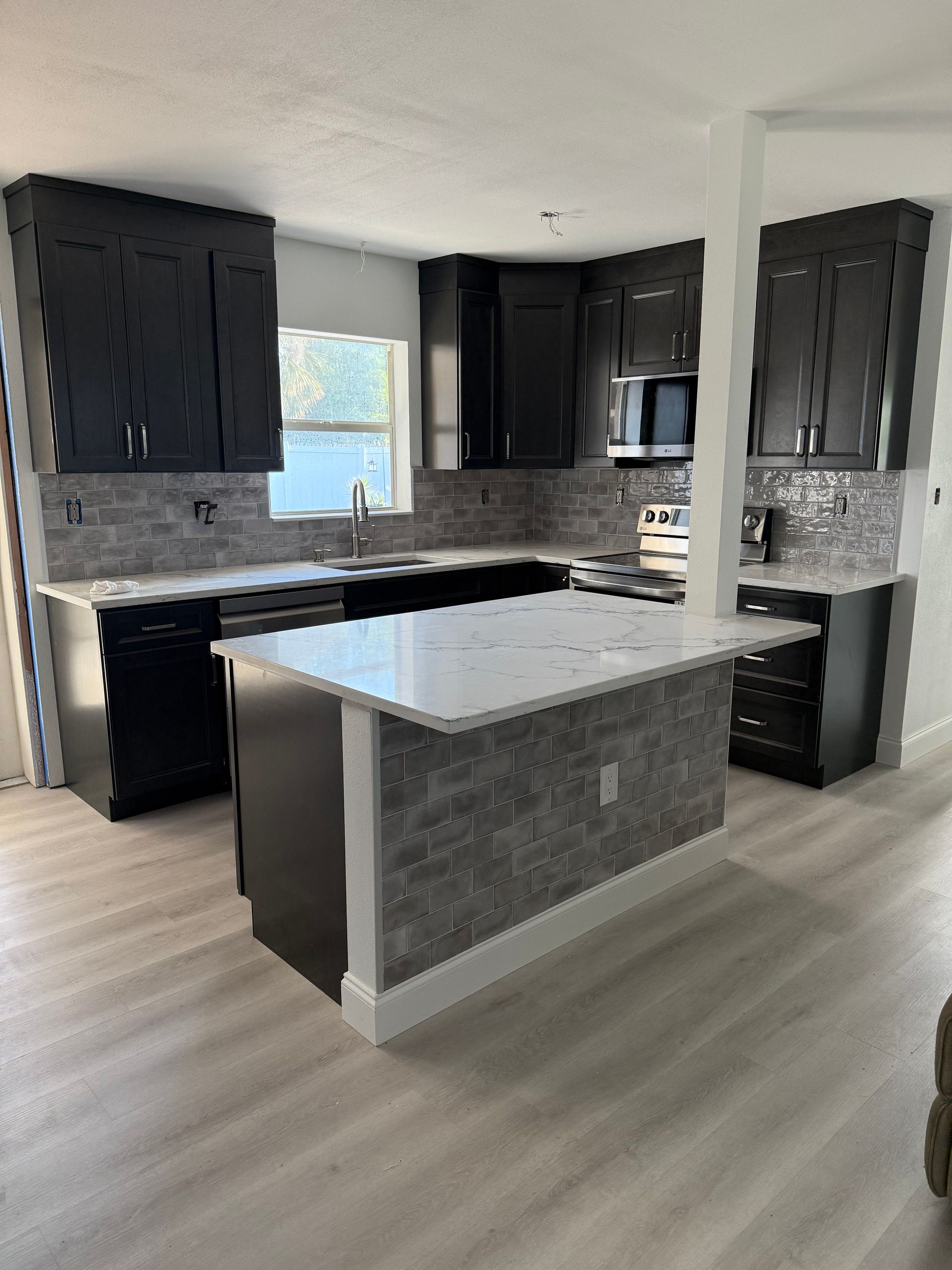 Modern kitchen with dark cabinets, gray tile backsplash, and a white island with granite countertop.