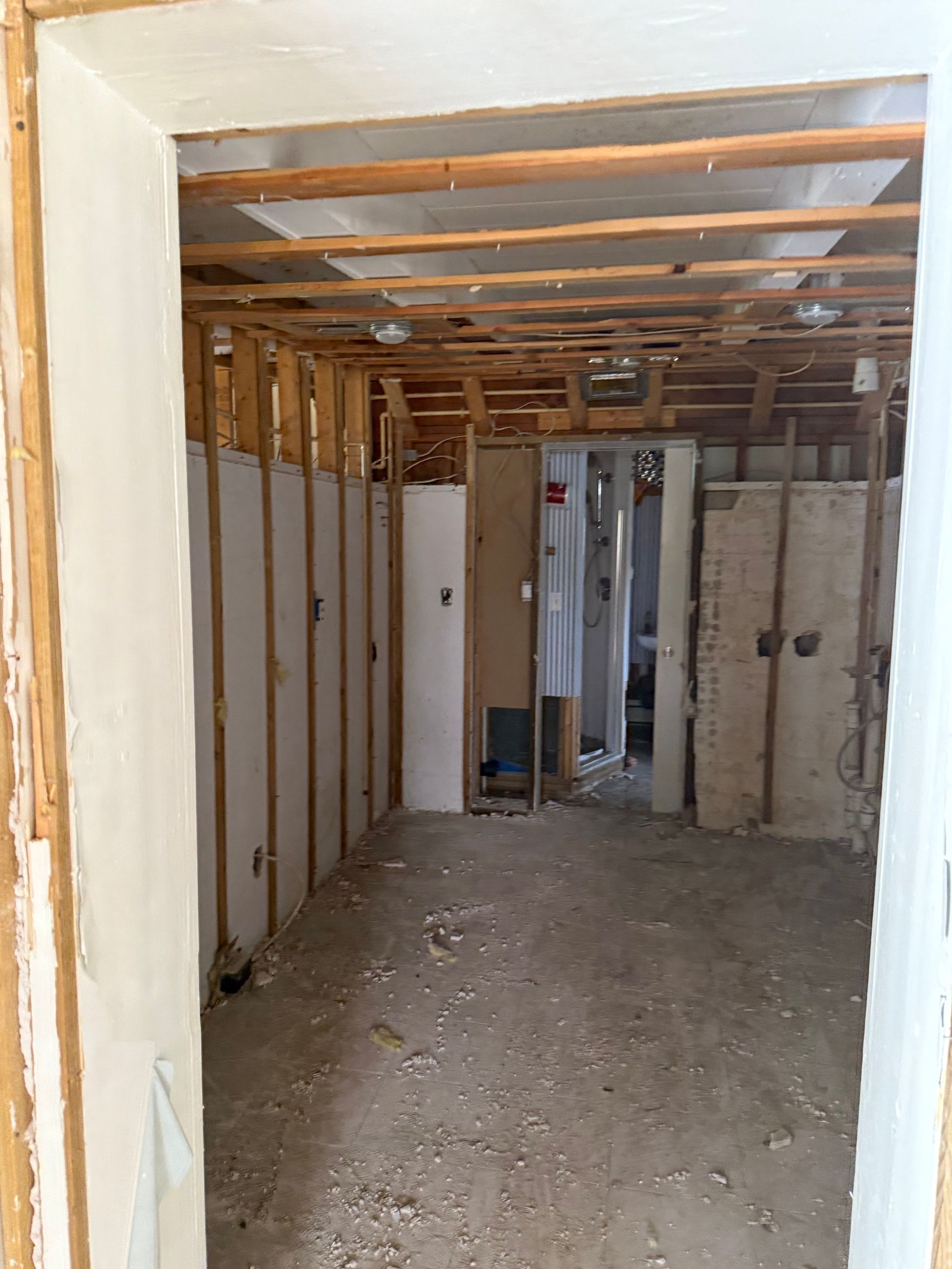 Unfinished room with exposed wooden framing, drywall panels, and a dirt floor seen through a doorway