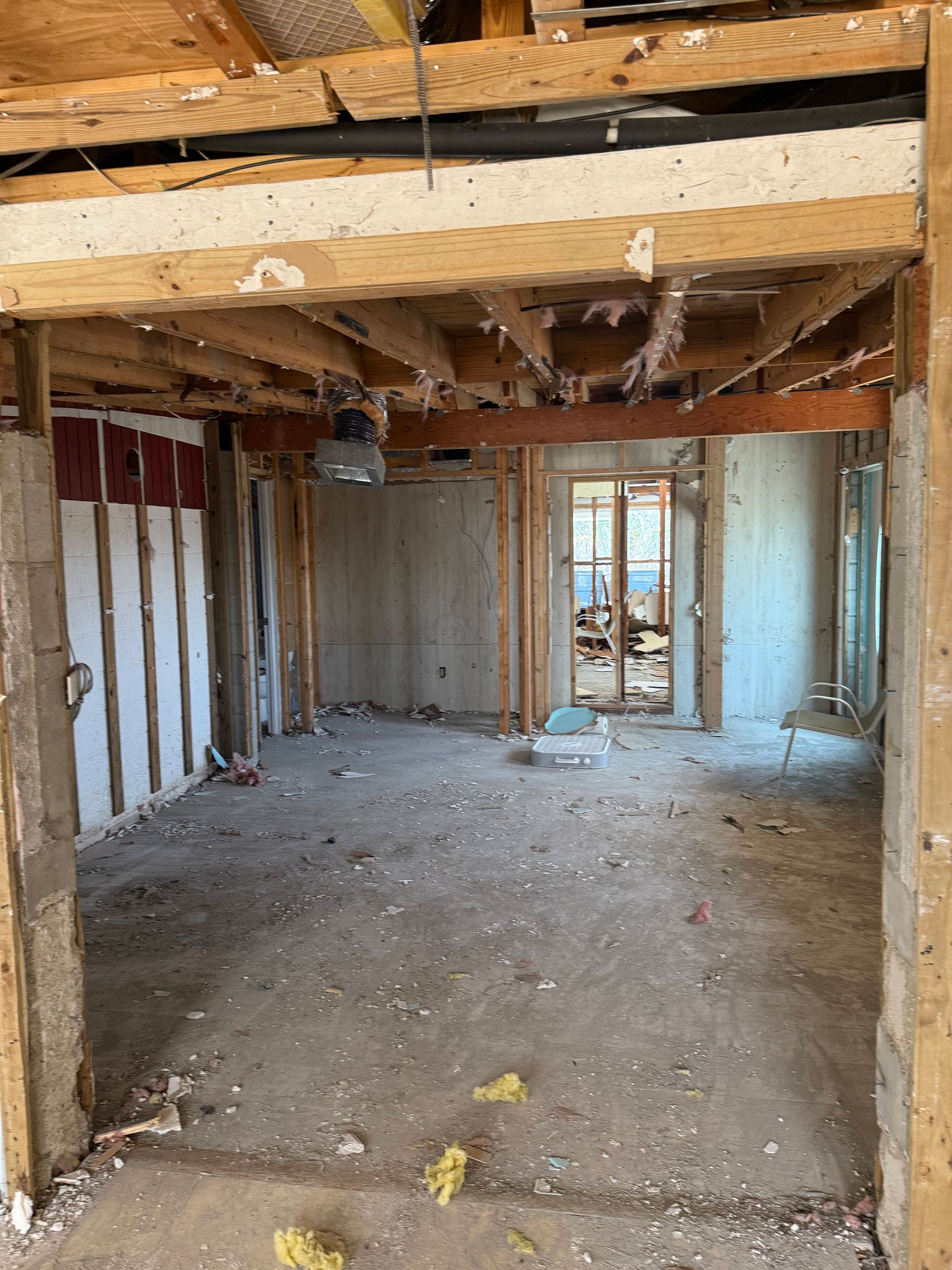 Interior of a gutted room under renovation, with exposed studs, insulation, and debris on the floor.