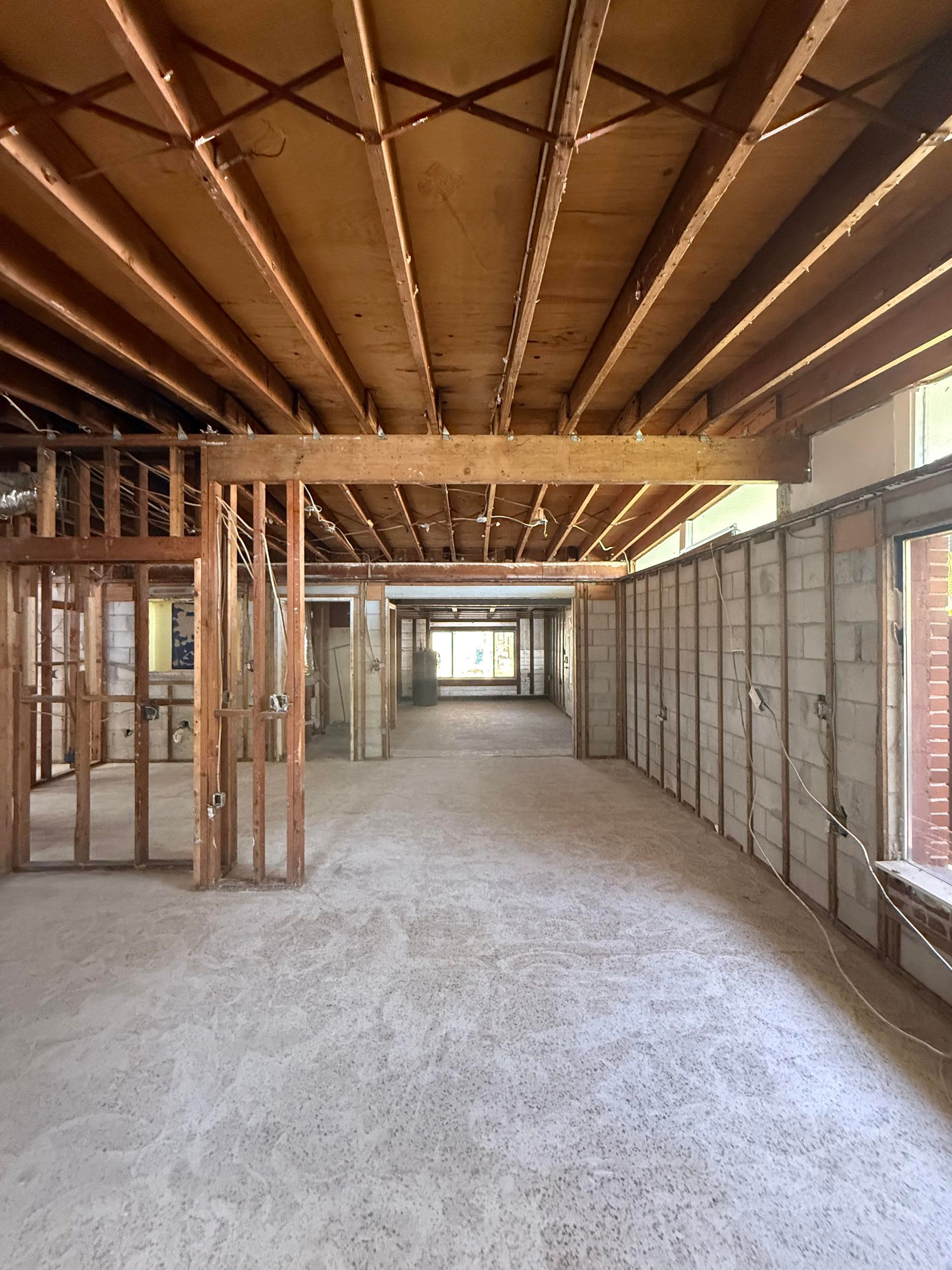 Unfinished interior with exposed wood framing, concrete floor, and brick walls in a long hallway