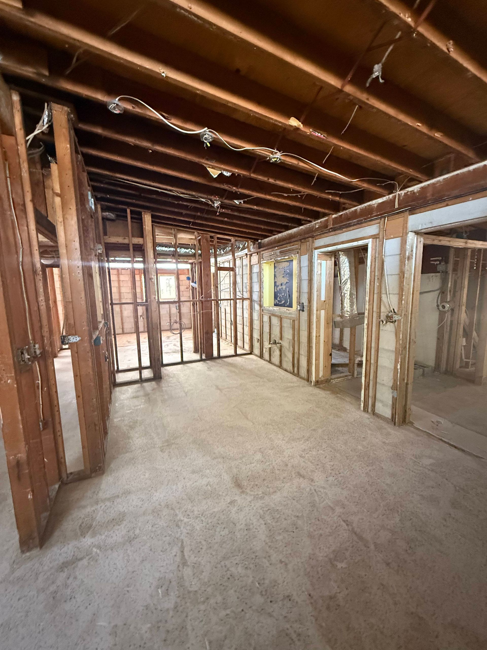 Unfinished house interior with exposed wood framing, open doorways, and bare concrete floor