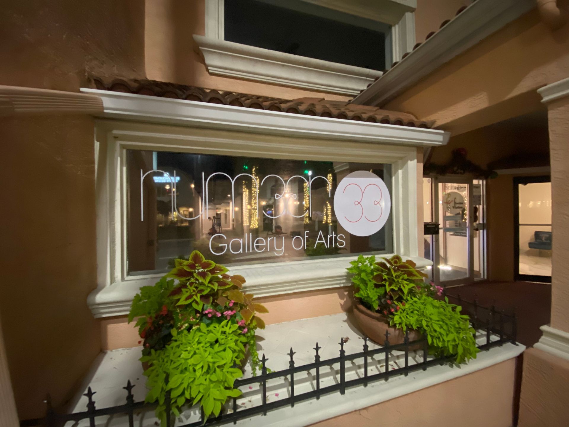 Gallery of Art storefront window with illuminated sign and planter boxes at dusk