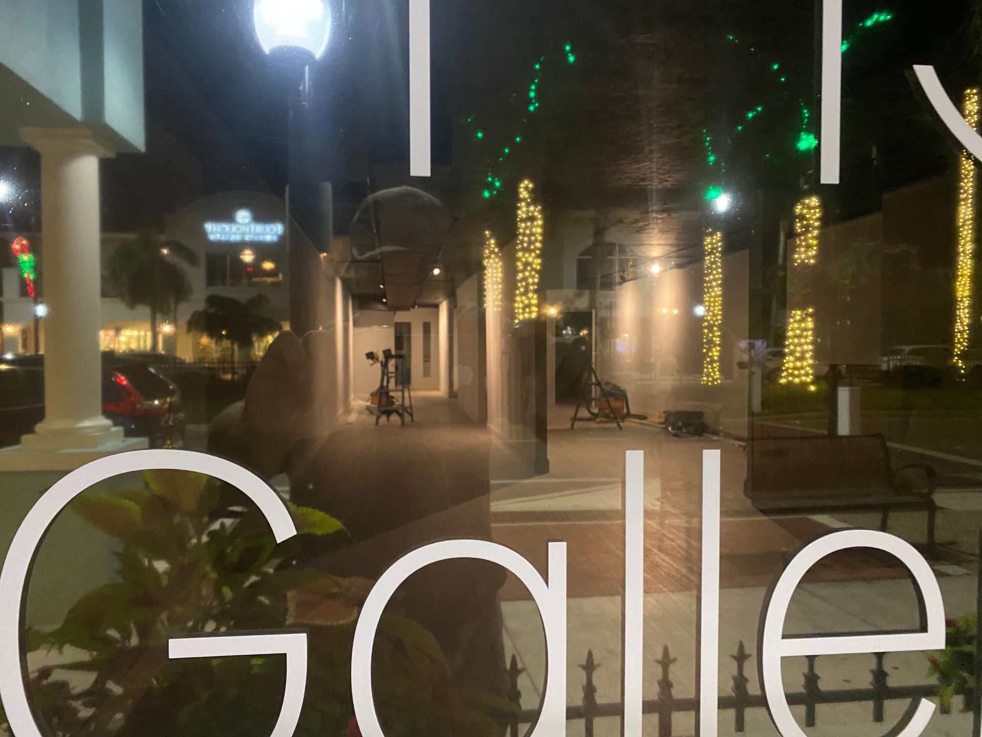 Nighttime walkway with lit palm trees and a bicycle under large “Gale” sign.