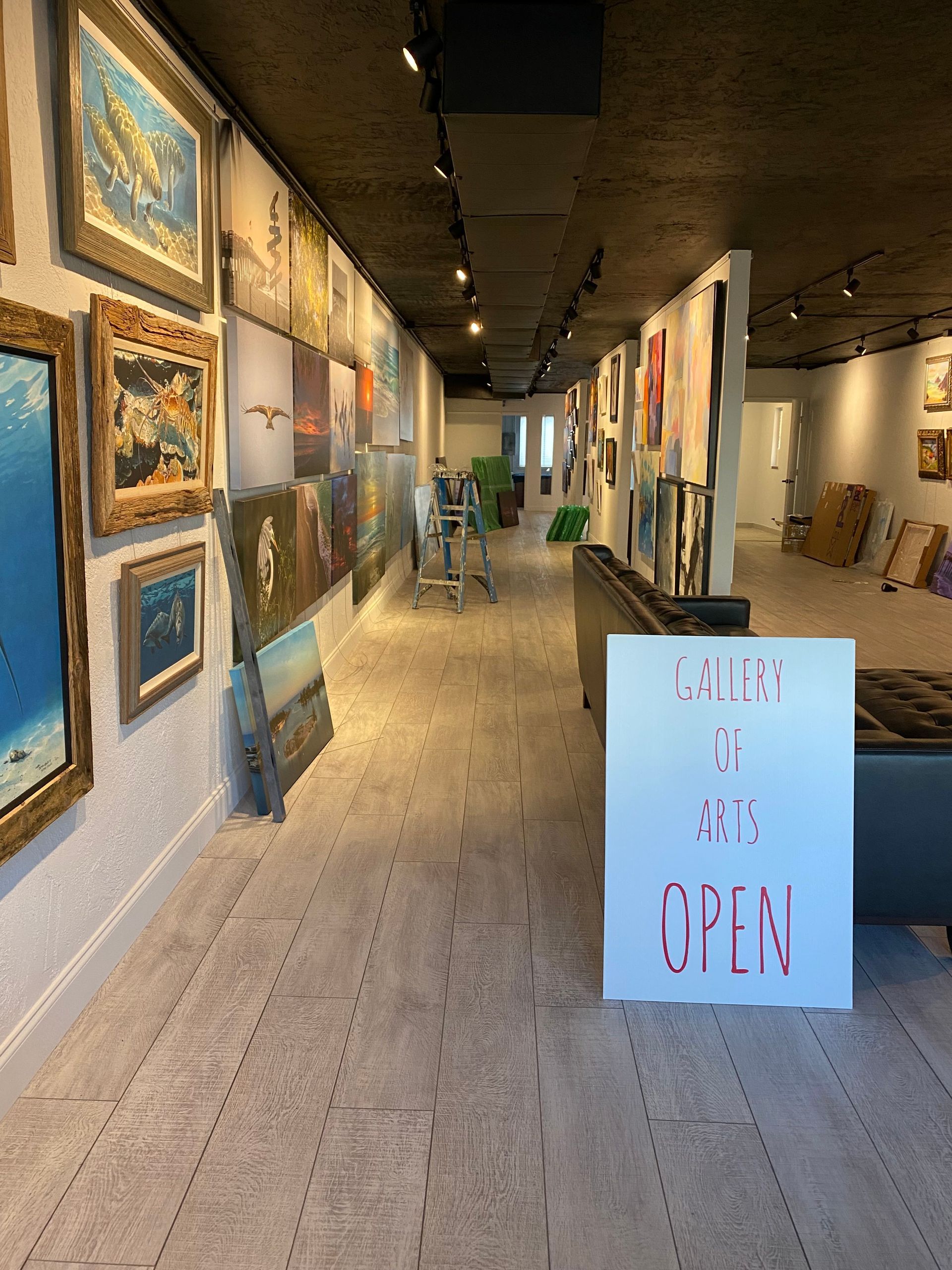 Art gallery hallway with framed paintings on both walls and an “OPEN” sign near the entrance