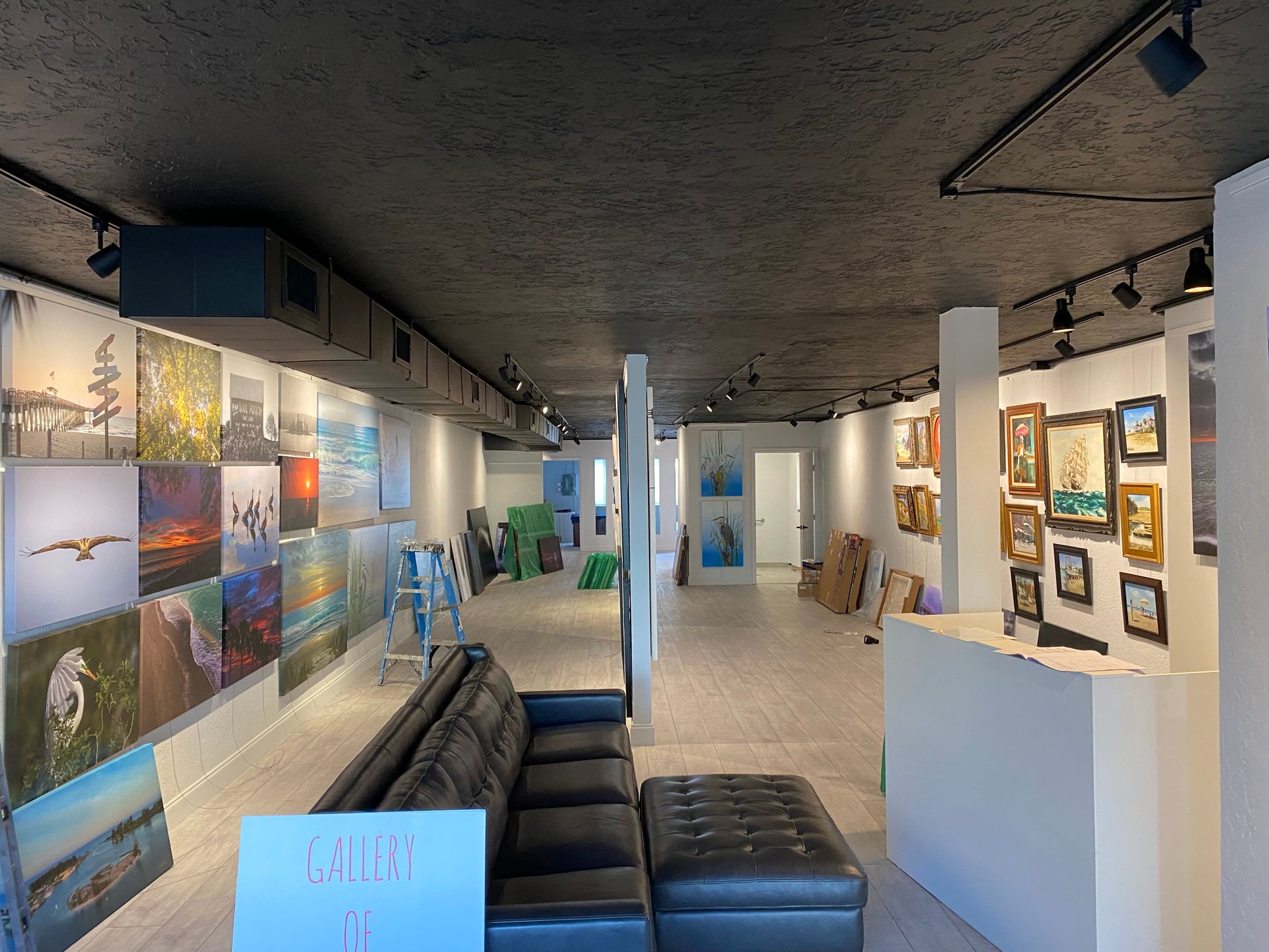 Art gallery interior with wall-mounted photos, white display walls, and black seating under a concrete ceiling