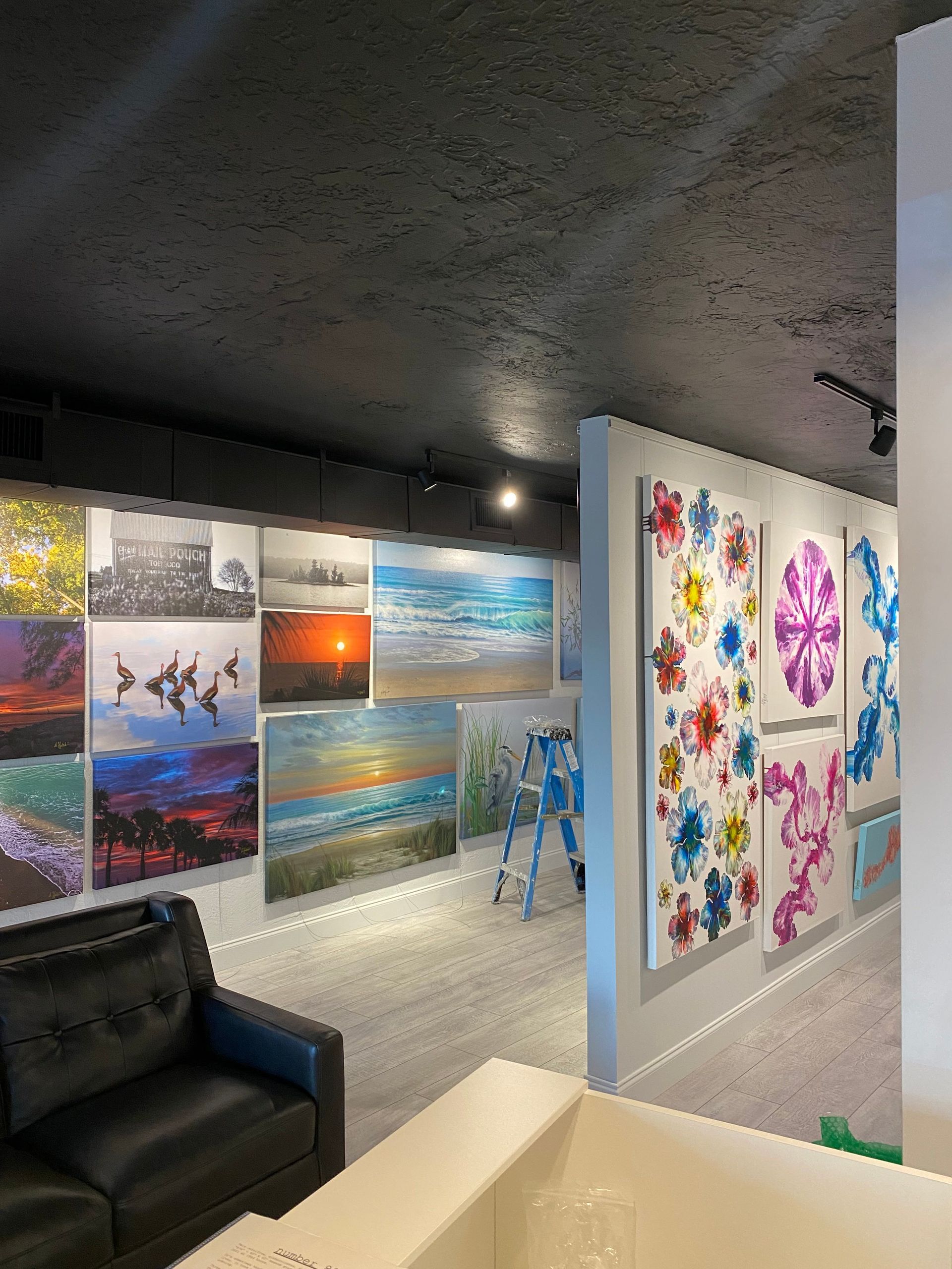Art gallery hallway with colorful paintings on dark walls and a black couch in the foreground.