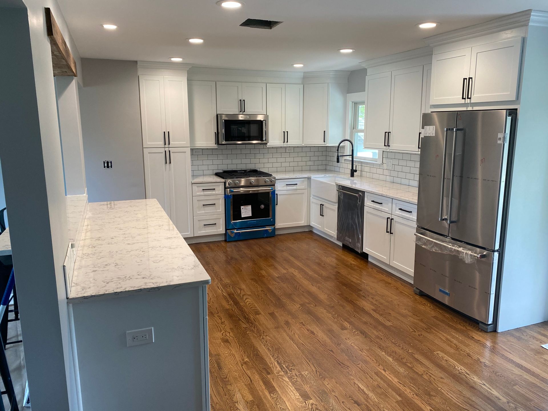 Bright modern white kitchen with stainless appliances, wood floor, and gray tile backsplash