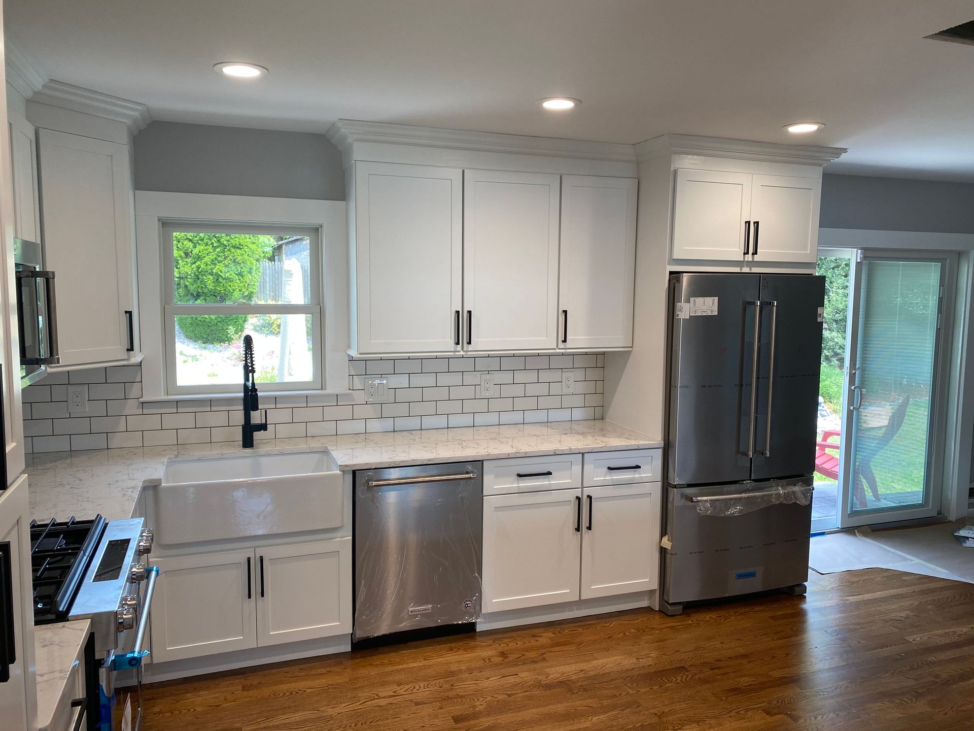 Modern kitchen with white cabinets, gray tile backsplash, stainless appliances, and wood flooring