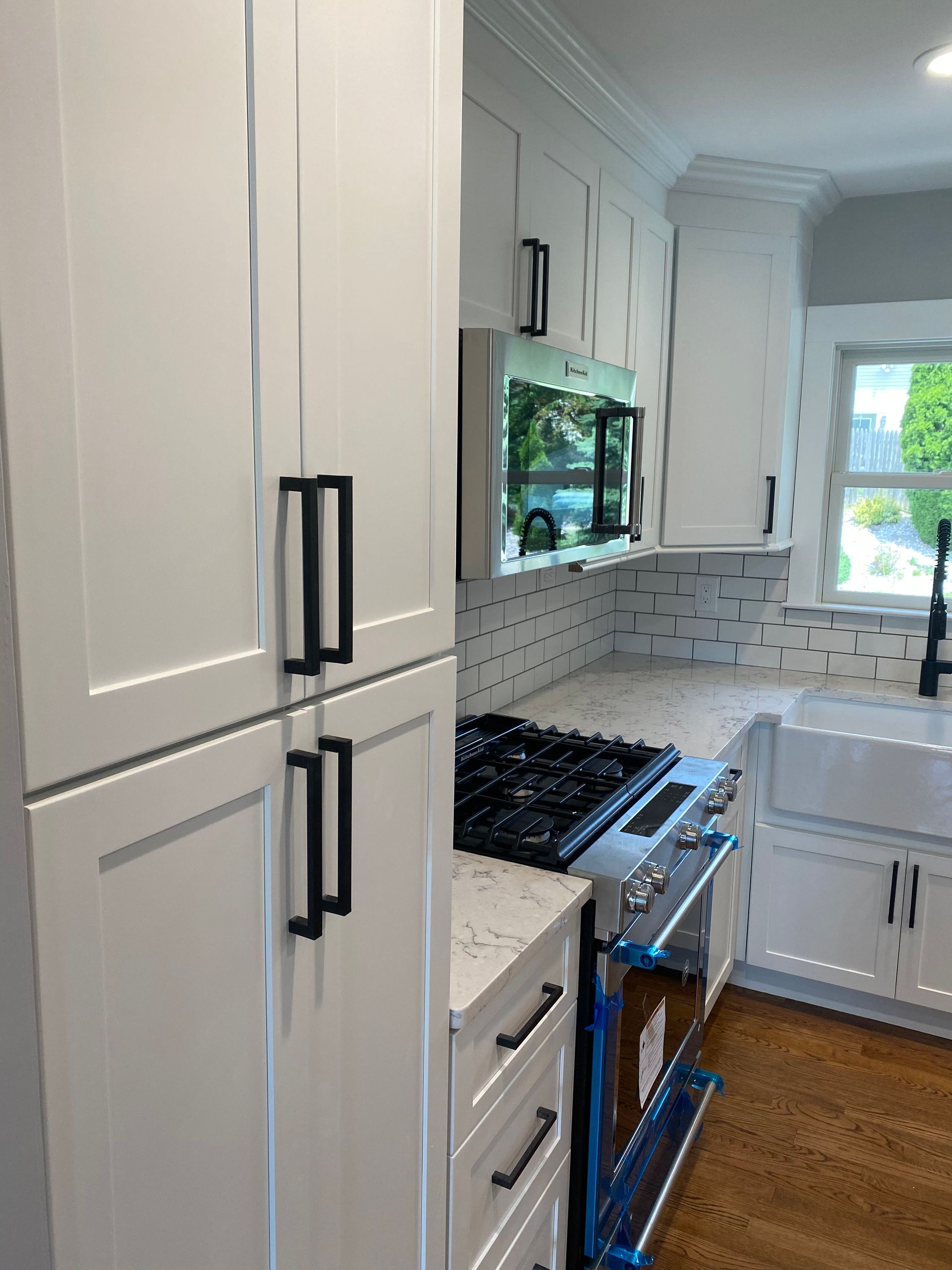 Bright modern kitchen with white cabinets, black handles, stainless stove, and a window over the sink.