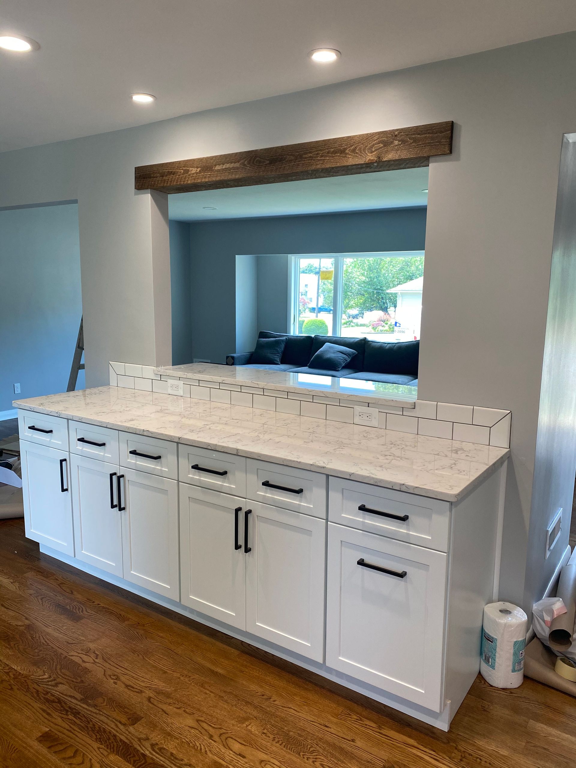 Kitchen with white cabinets, marble island countertop, and a pass-through window with a wood beam trim.