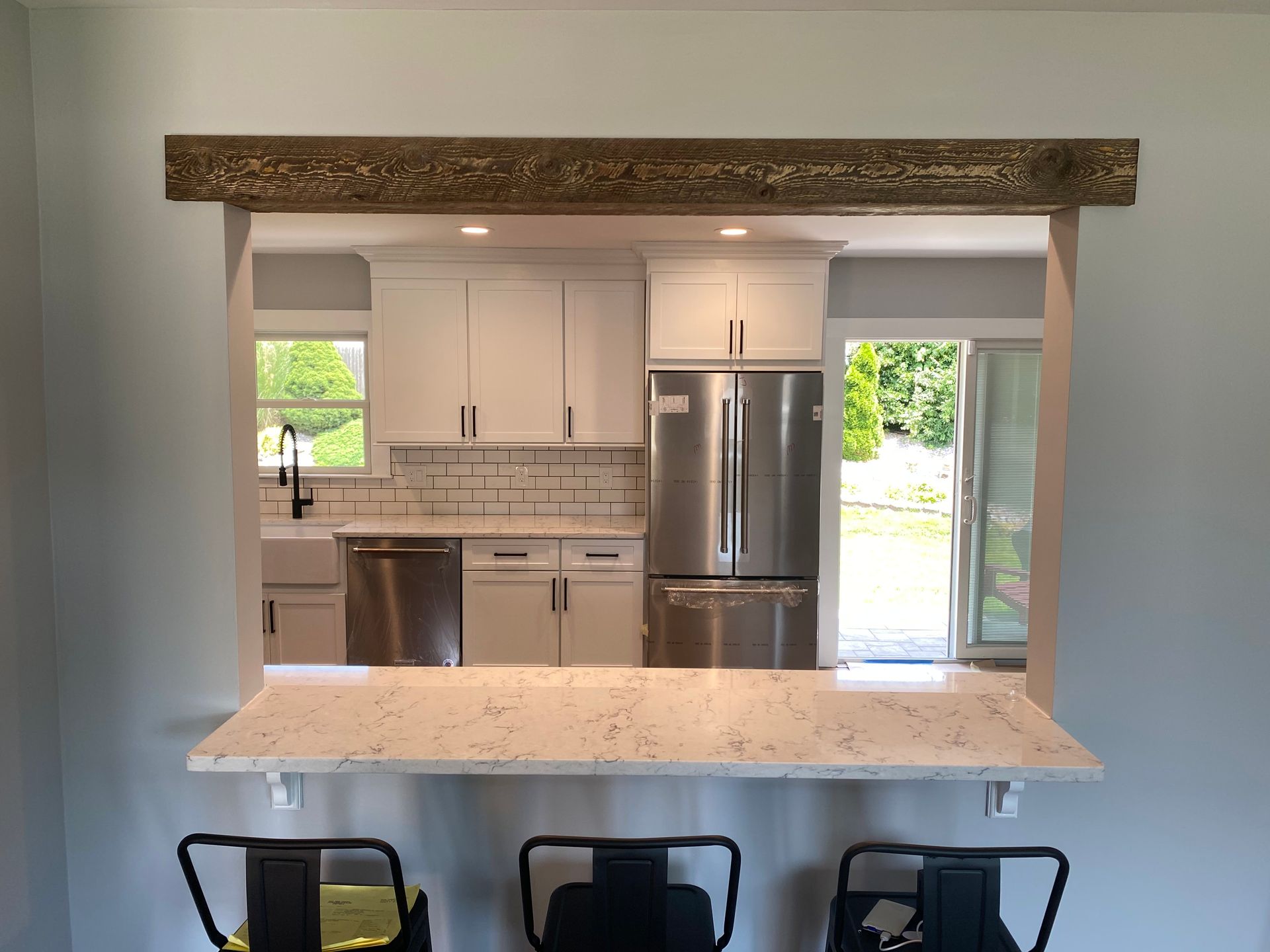 View through a kitchen pass-through to a bright white kitchen with stainless-steel appliances and a granite counter.