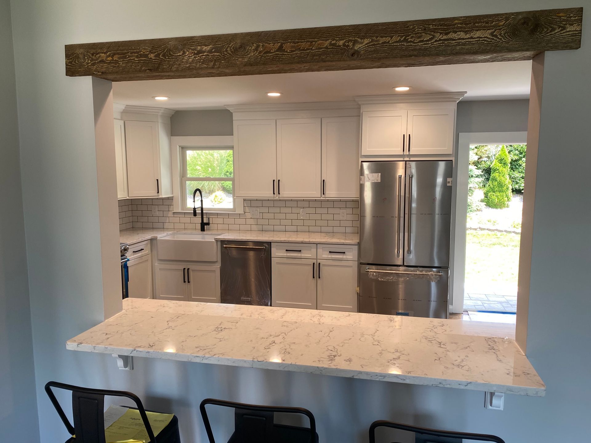 Bright kitchen with white cabinets, stainless appliances, marble island, and exposed wood beam.