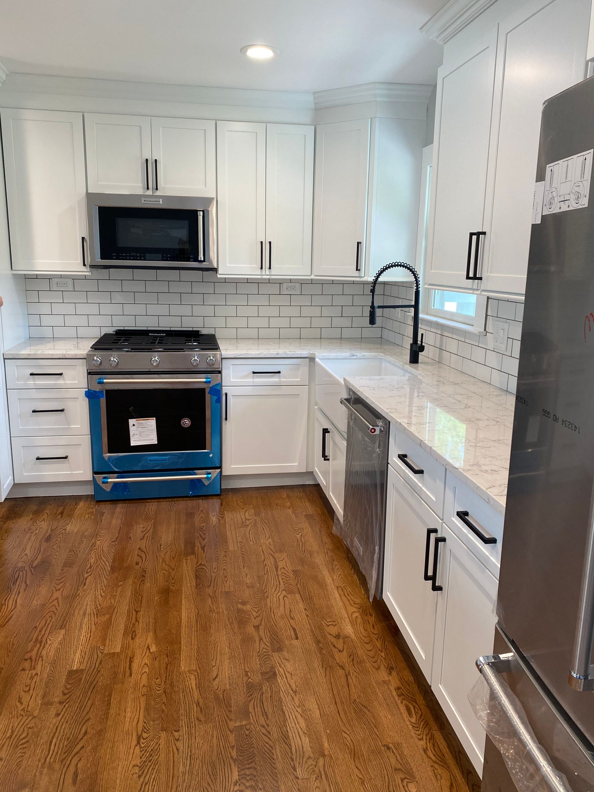 Bright white galley kitchen with stainless appliances, black countertops, and wood floors