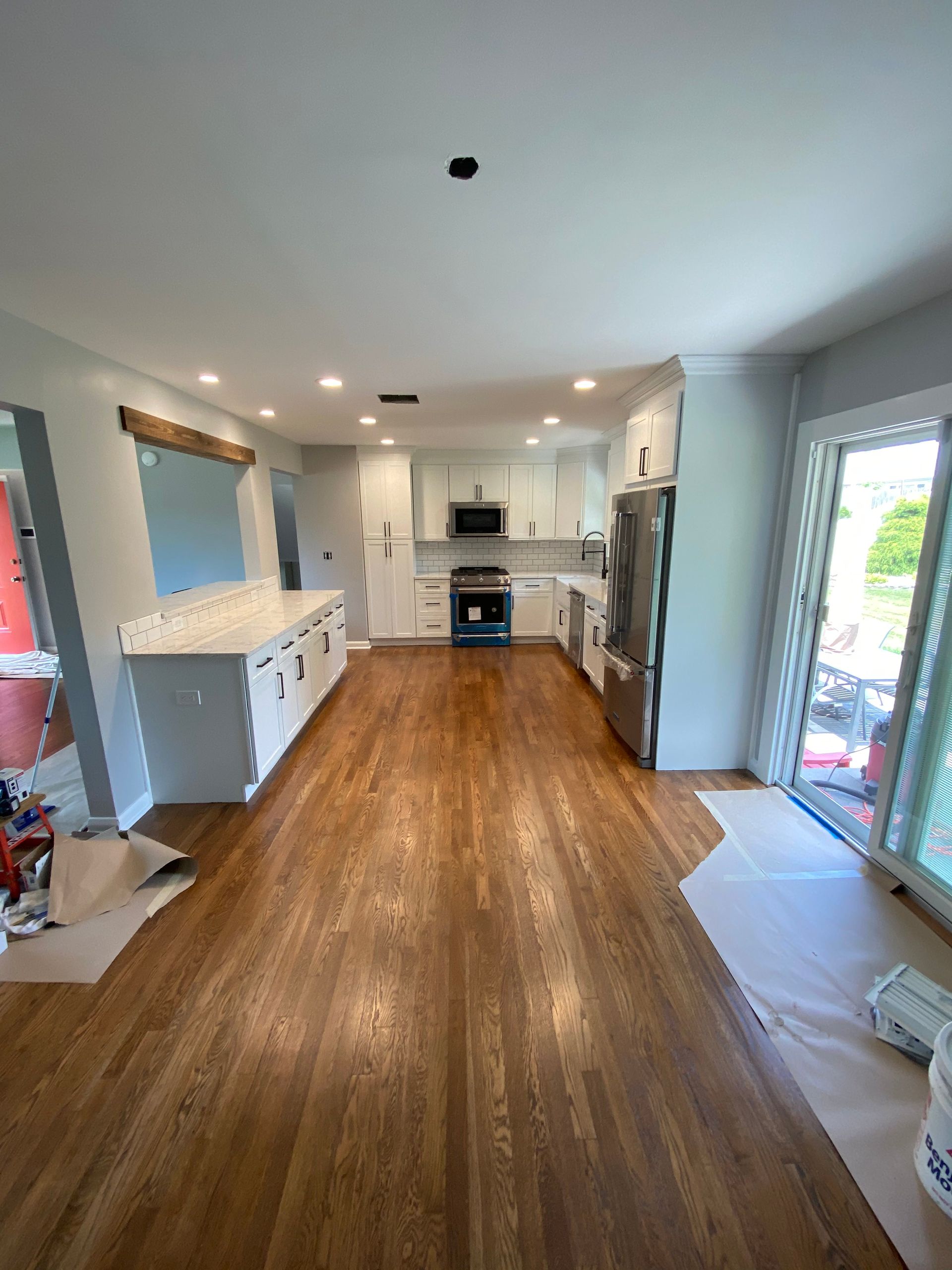 Empty modern kitchen with wood floors, white cabinets, stainless fridge, and sliding glass doors to a patio